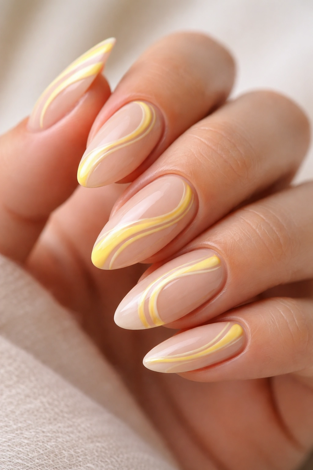 Close-up of almond nails with pale base and yellow swirls leaving negative space