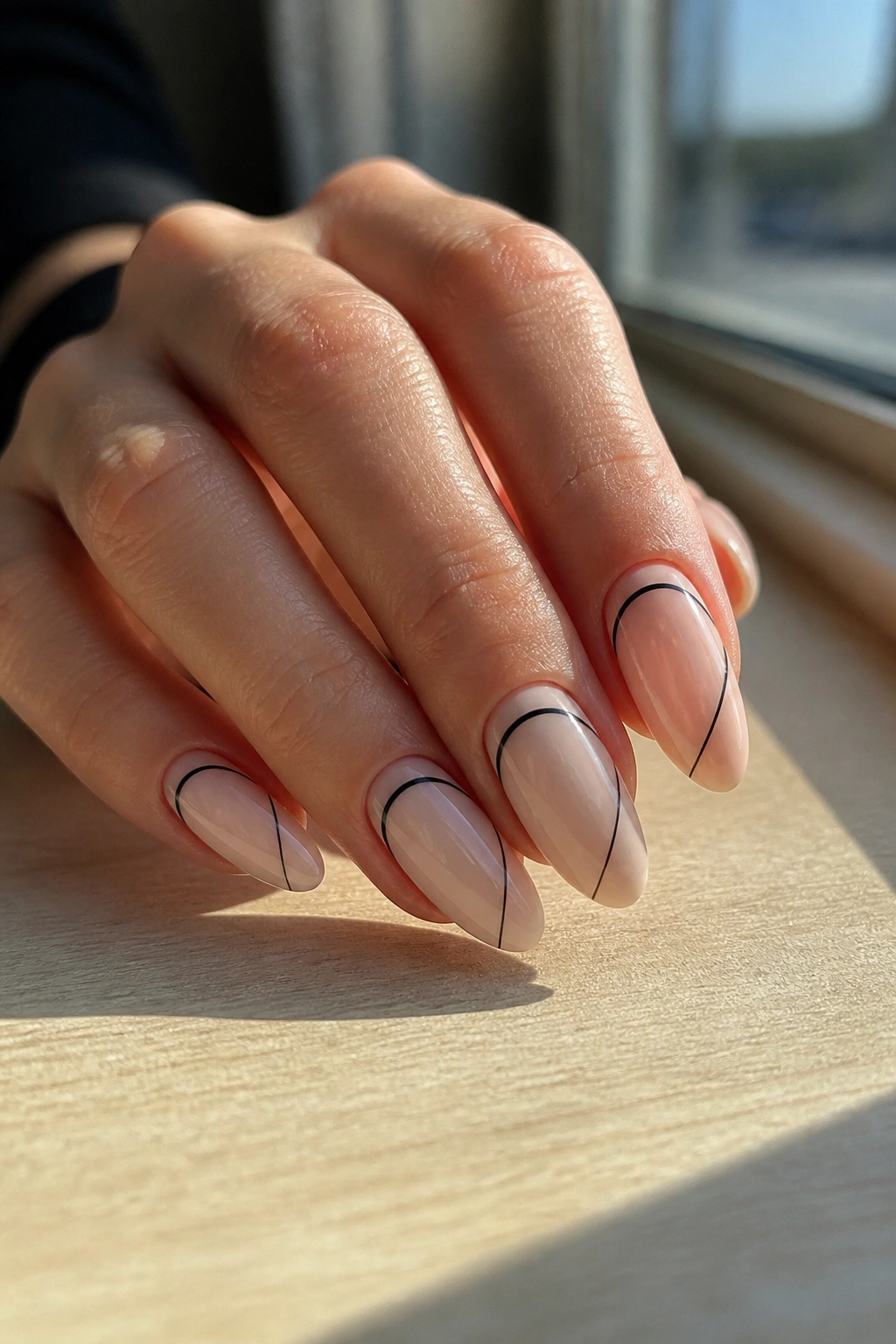 Close-up of almond nails with abstract black line art on pale base