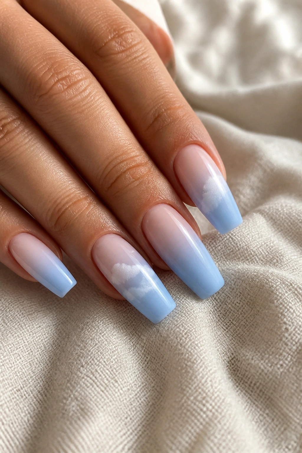 Nails with pale blue ombre and soft white clouds on real hand