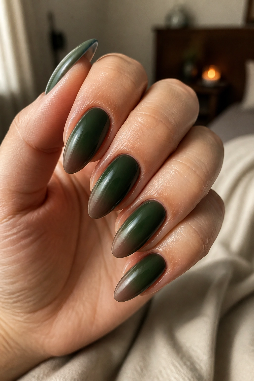 Close-up of almond nails with a dark green aura fade on a real hand