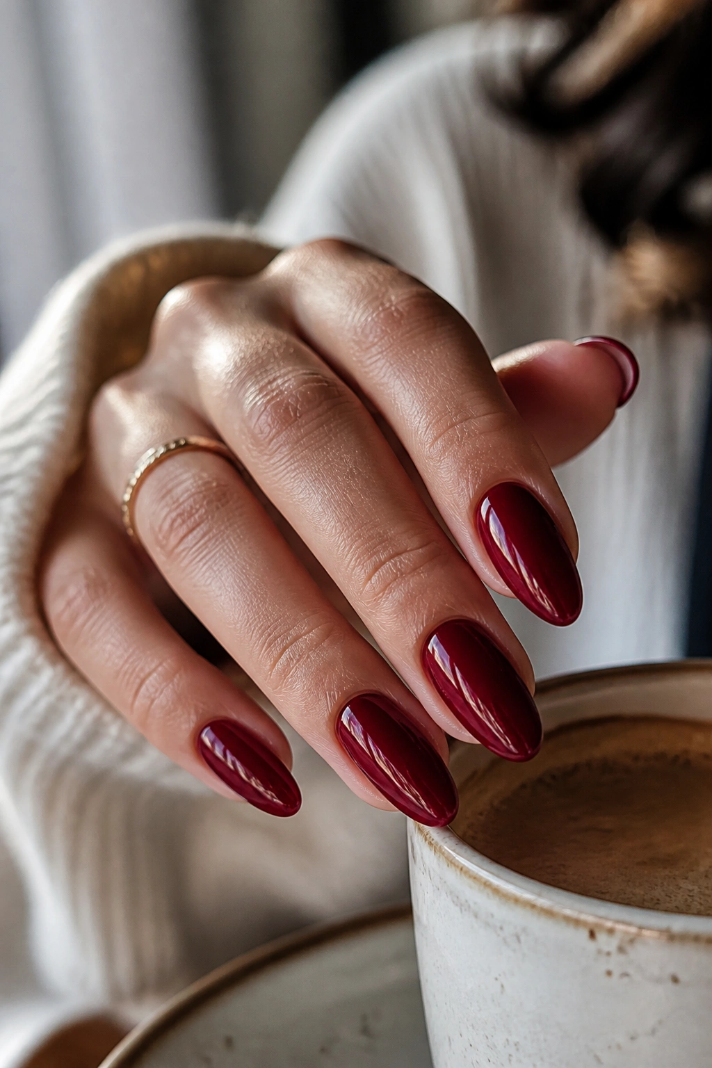 Close-up of deep cherry red almond nails holding a coffee cup