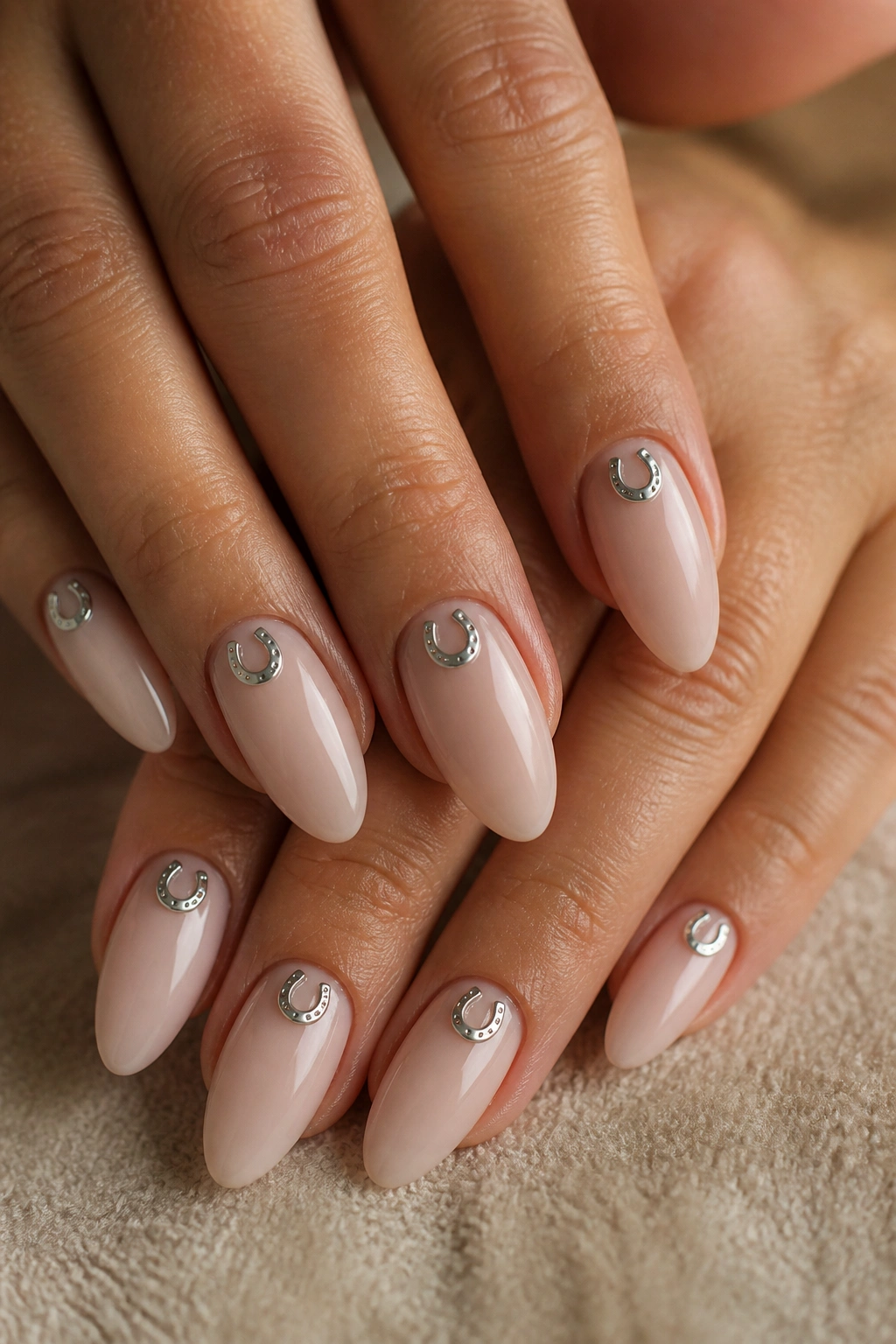 Close-up of nude almond nails with tiny silver horseshoes on real hands
