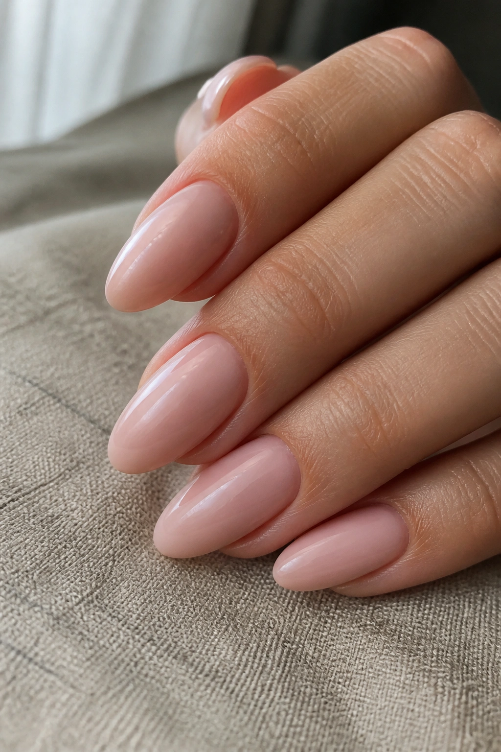 Close-up of almond nails in barely-there rose pink with glossy finish on a real hand