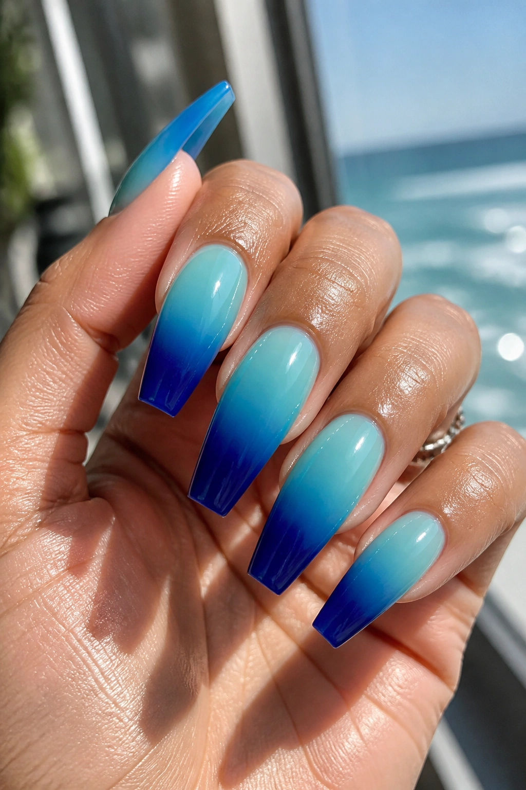 Close-up of aqua to cobalt glass fade coffin nails on a real hand with glassy finish