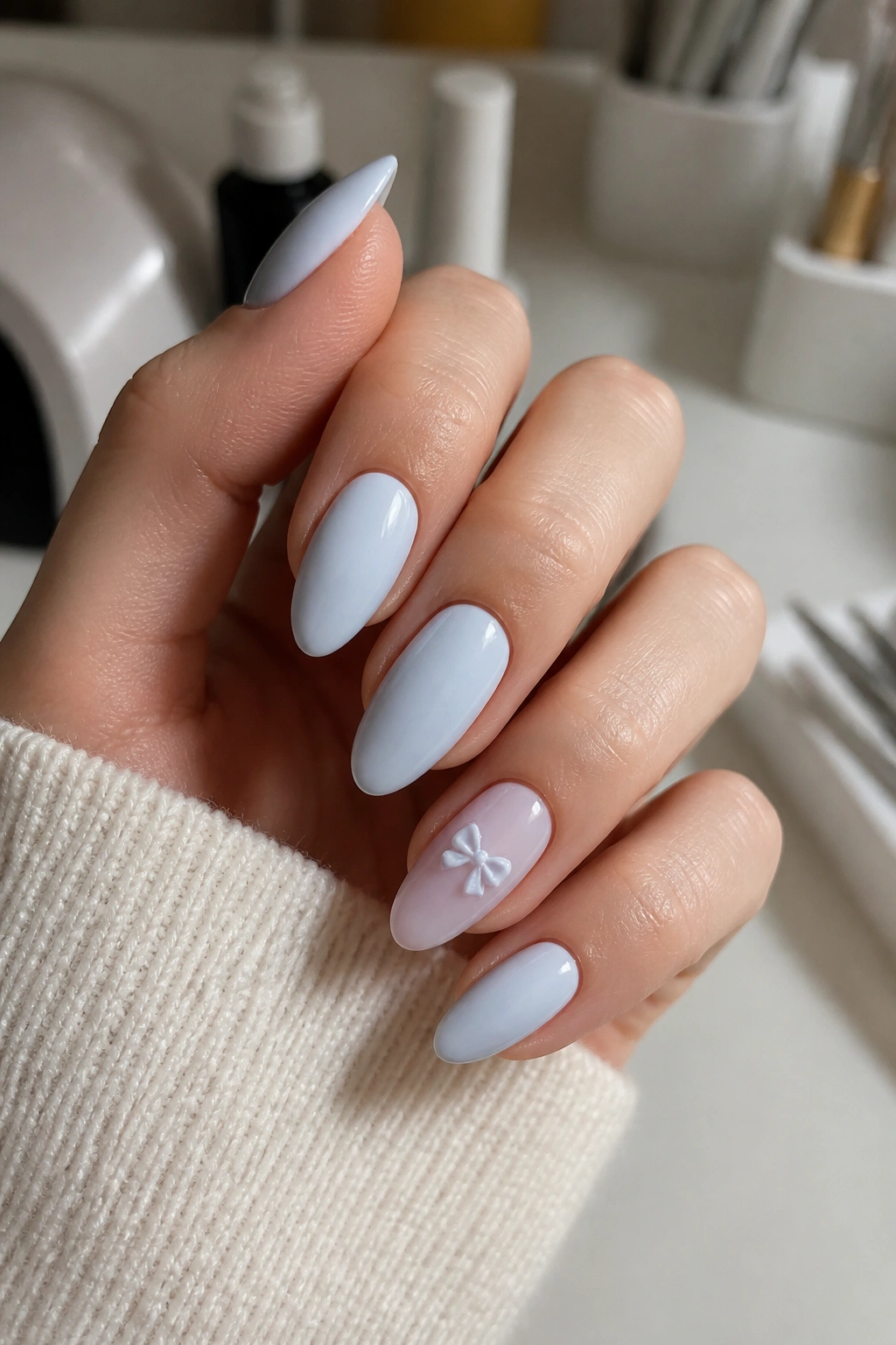 Close-up of hand with almond nails featuring a tiny baby blue bow on an accent nail