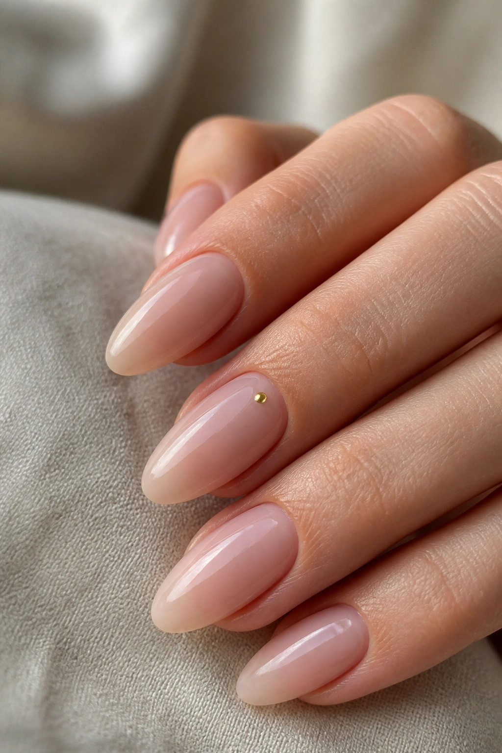 Close-up of bare beige almond nails with tiny gold dots on a real hand