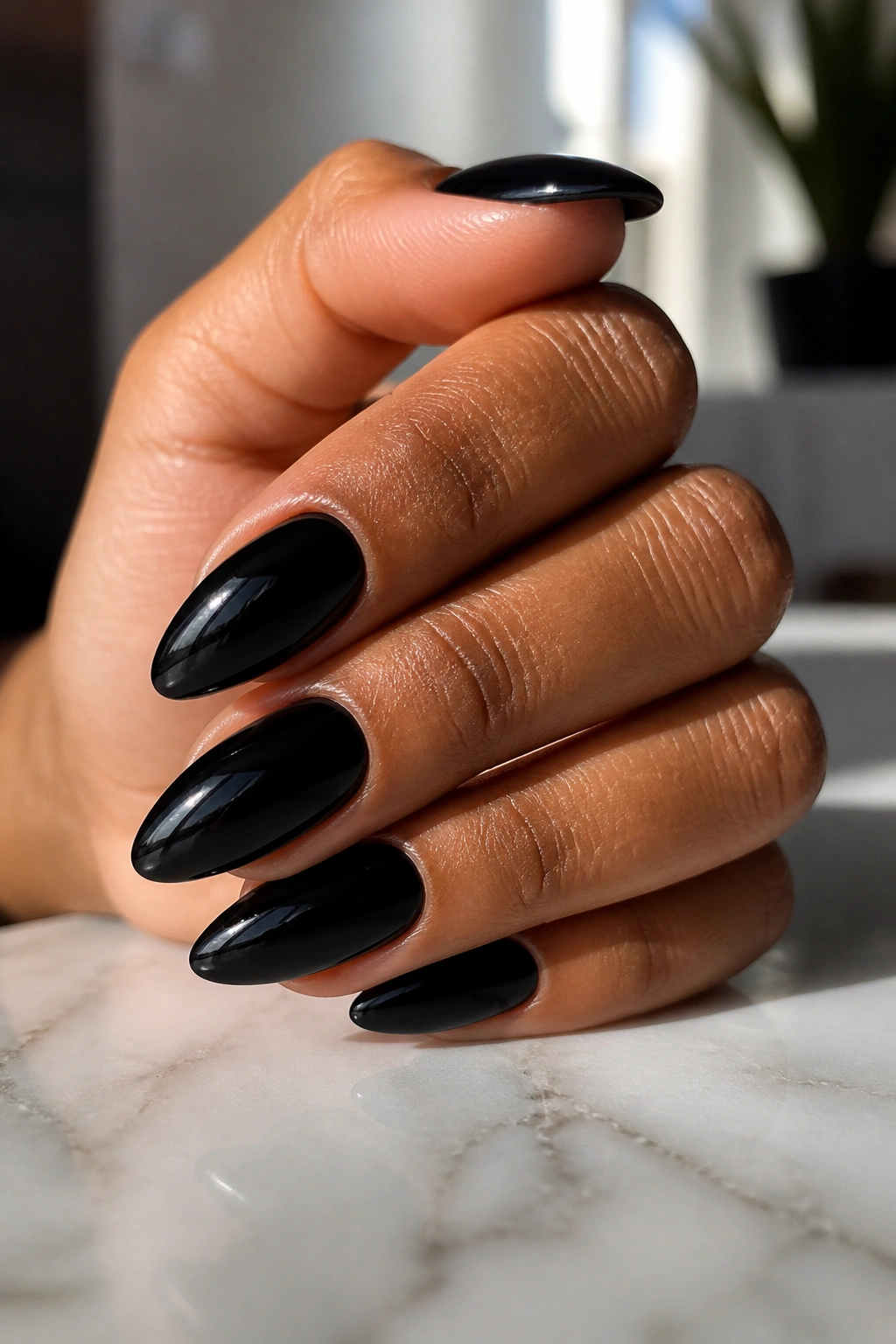 Close-up of a real hand with almond-shaped black nails, glossy finish