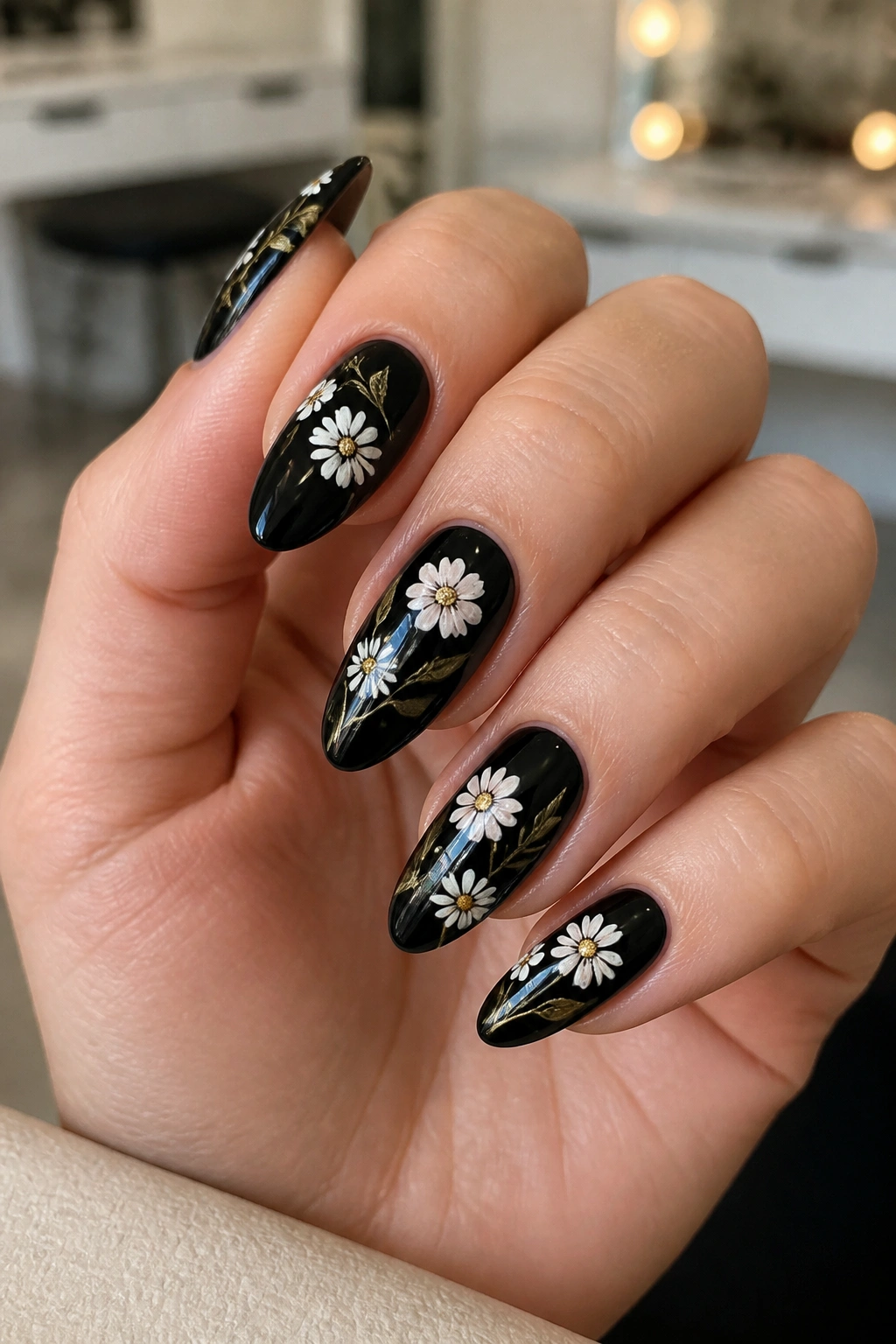 Close-up of black almond nails with white daisies and pale floral petals on a real hand