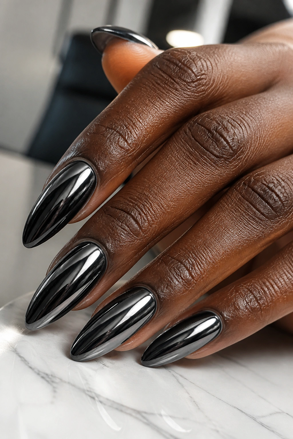 Close-up of black chrome almond nails on a dark-skinned hand with reflective metallic finish