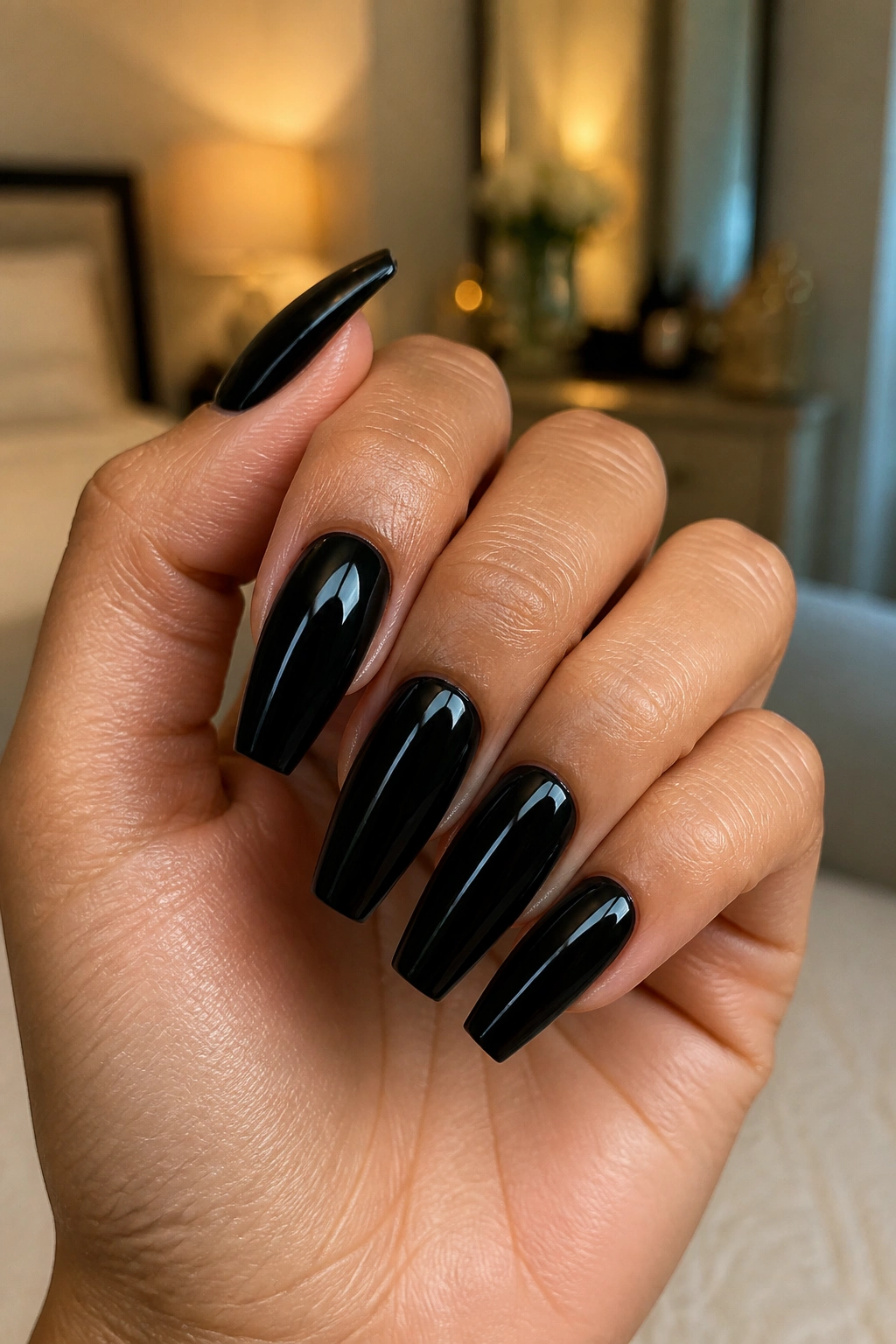 Close-up of glossy black coffin nails on a real hand in warm room light