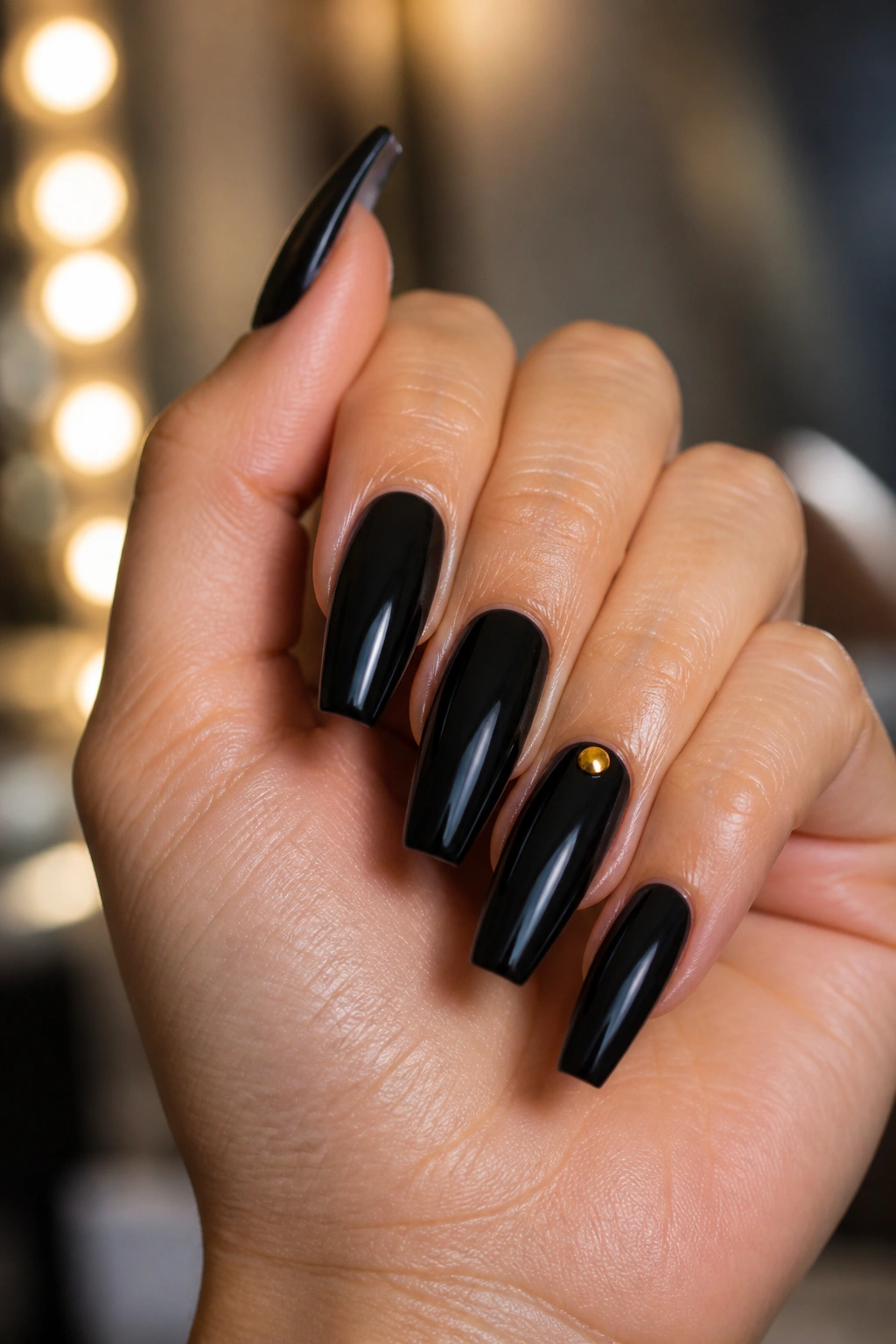 Close-up of black coffin nails with a gold stud on a real hand