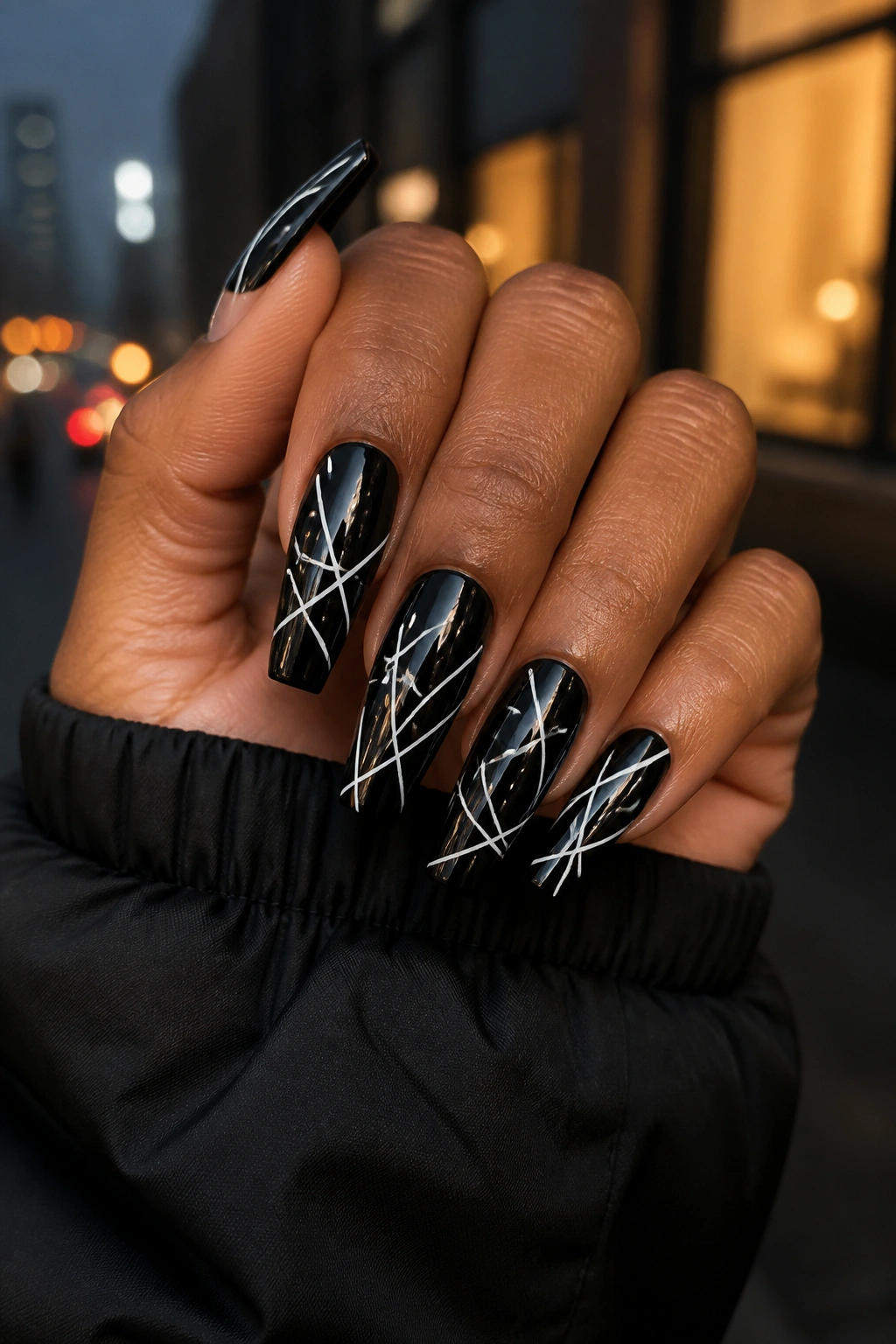 Close-up of black coffin nails with white graffiti lines on a real hand