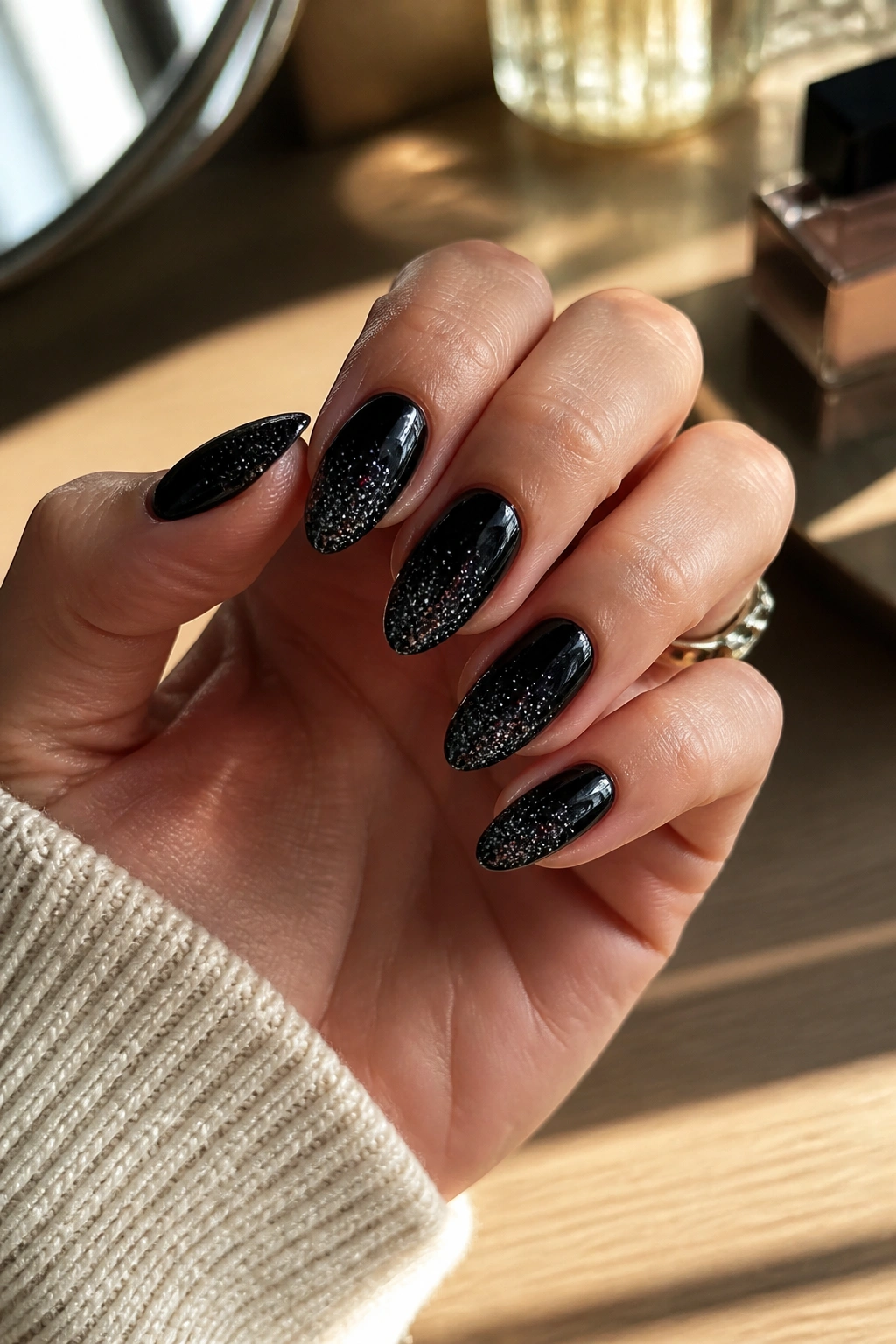 Close-up of almond nails with a black base and silver glitter on a real hand