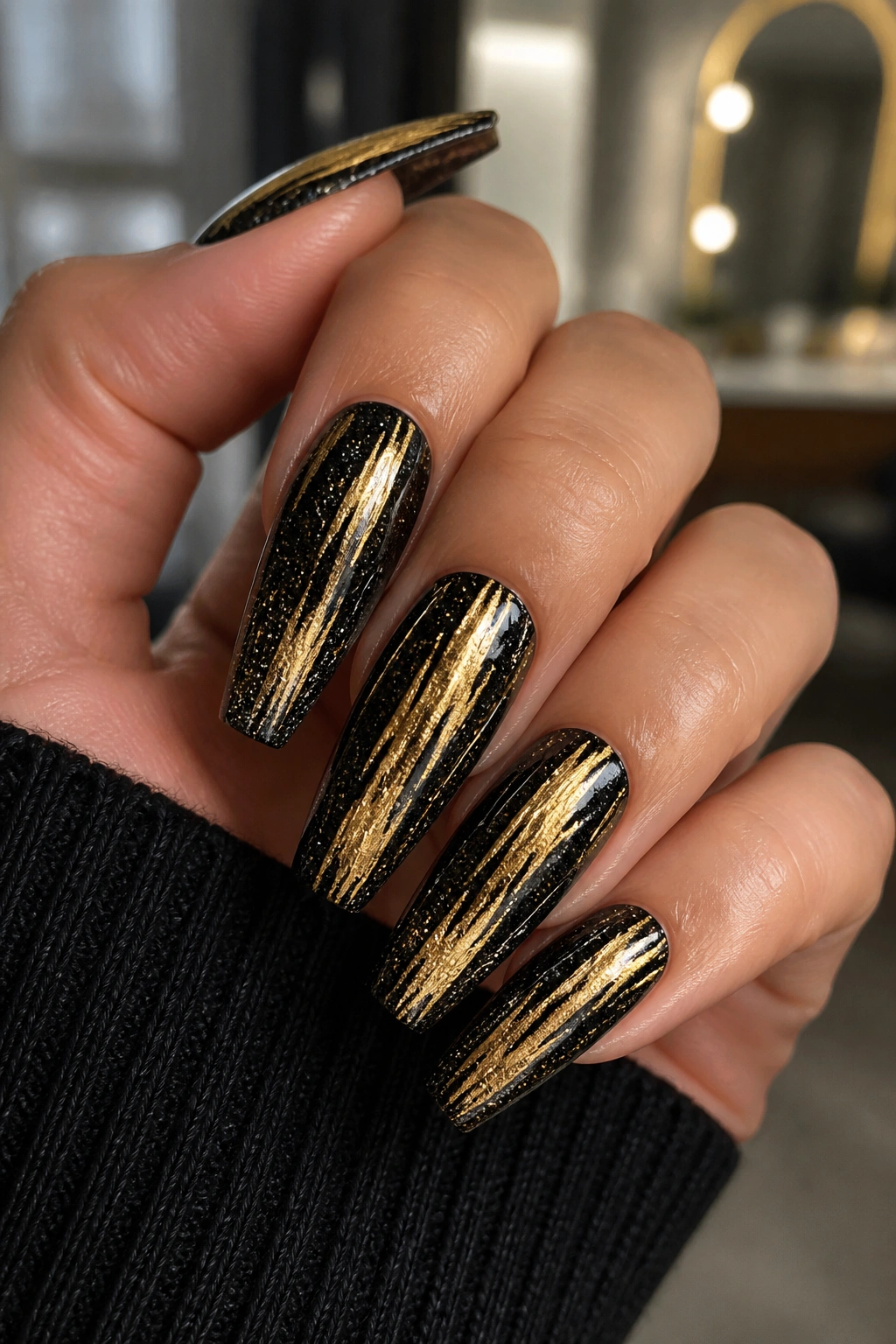 Close-up of coffin nails with black glitter and gold stripes on a hand