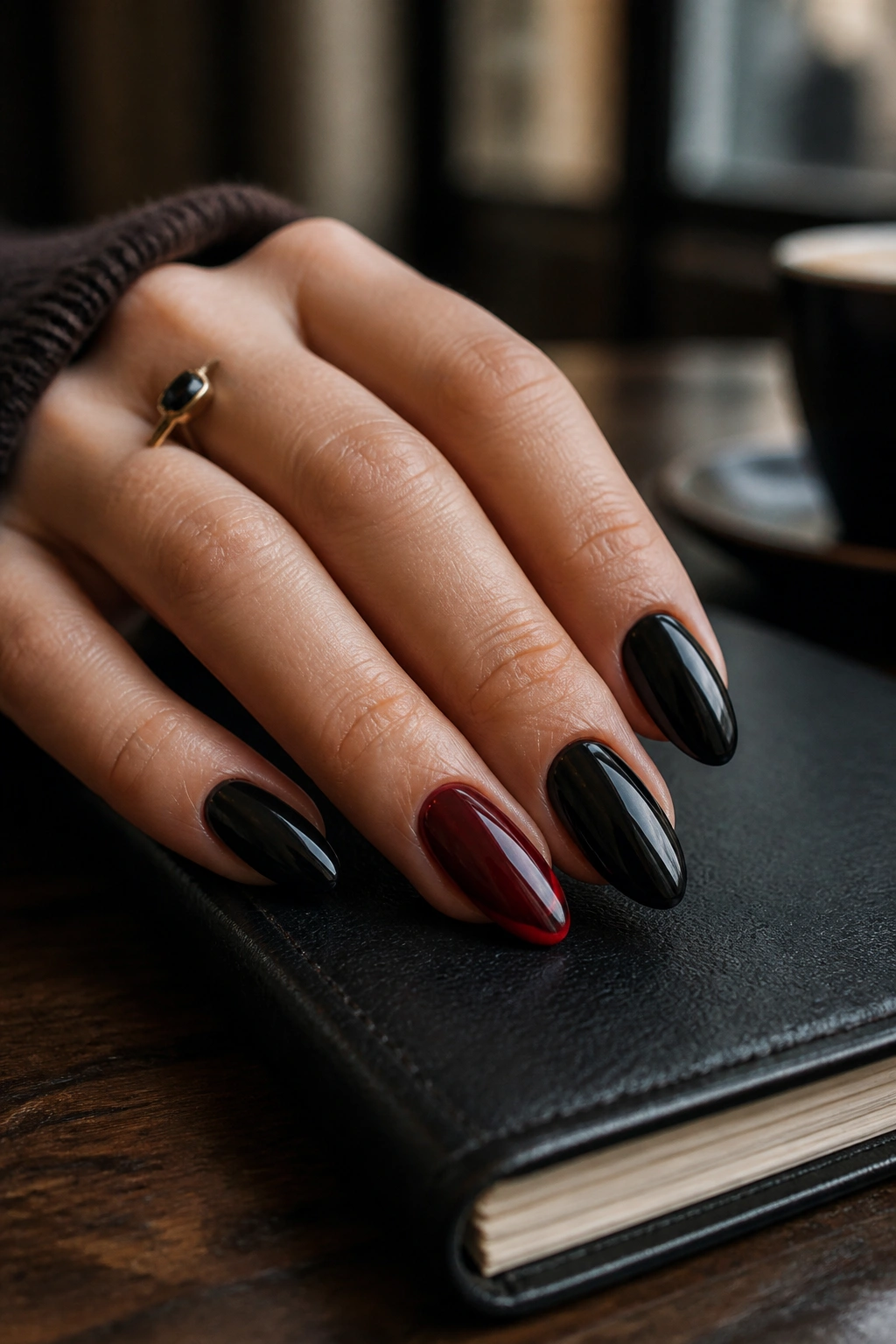 Close-up of almond nails with four black nails and a single oxblood accent nail on a moody cafe table