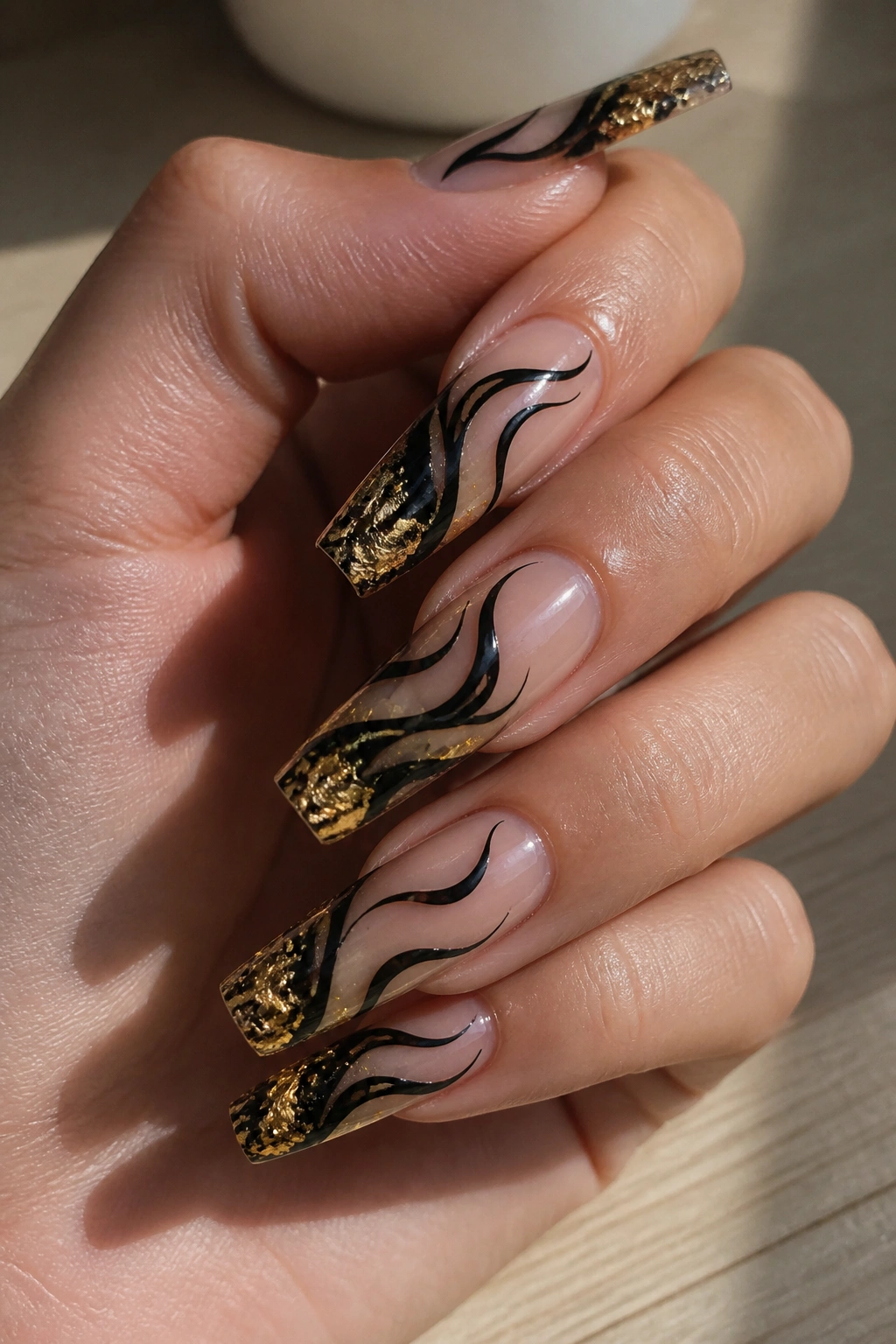 Close-up of black swirl nails with gold leaf tip on nude base