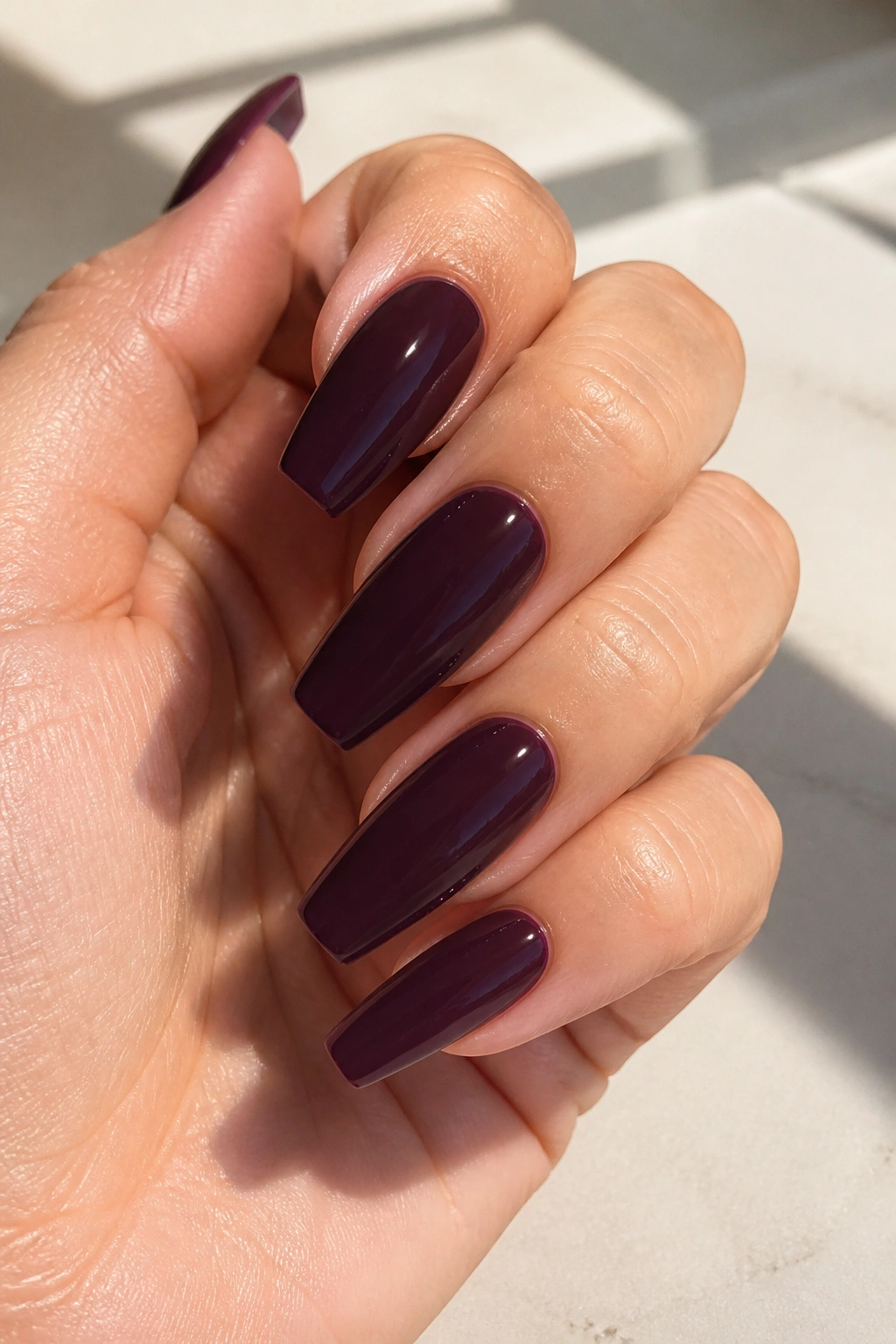 Close-up of blackberry cream coffin nails on real hand with soft sunlight