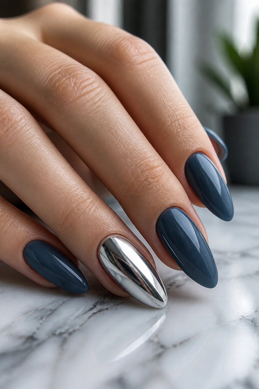 Close-up of almond nails in deep slate blue with a chrome accent nail on a real hand