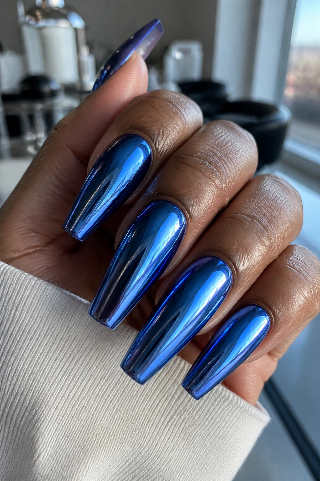 Close-up of blue chrome coffin nails on a real hand with sharp coffin tips.