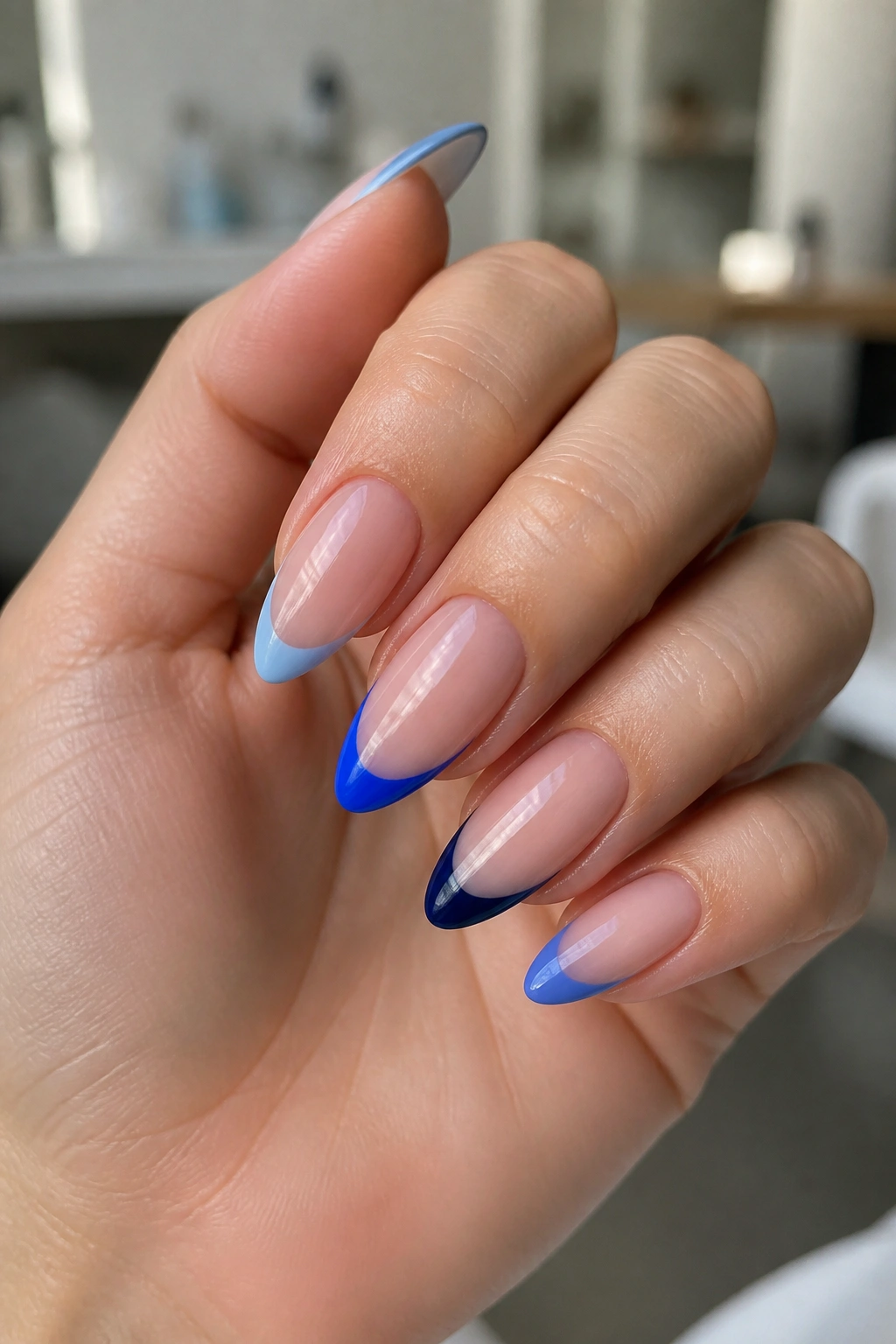 Close-up of mixed-shade blue French tip almond nails on a real hand with a sheer pink base