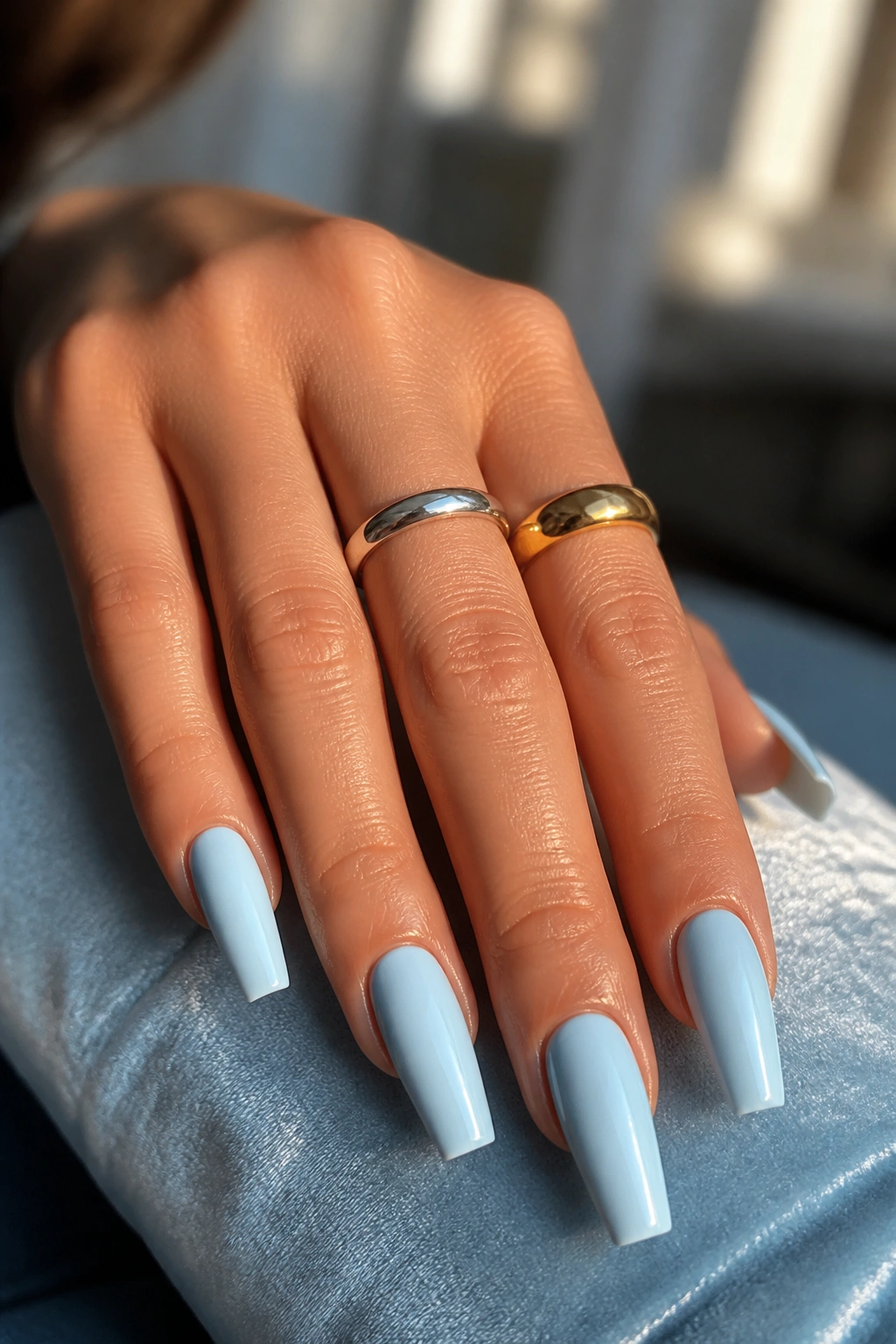 Close-up of a real hand with icy blue coffin nails, showing skin tone variation and mixed-metal rings.