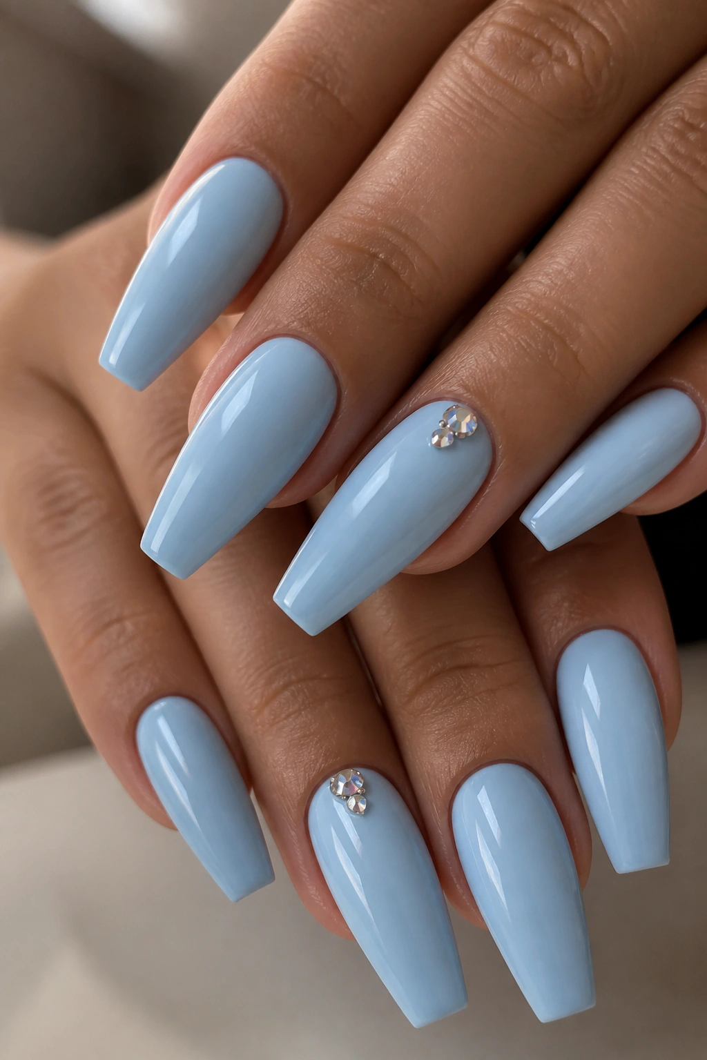Close-up of light blue coffin nails with tiny rhinestone clusters near the cuticle