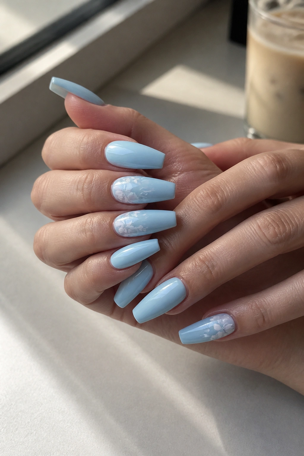 Close-up of light blue coffin nails with white floral details on two accent nails