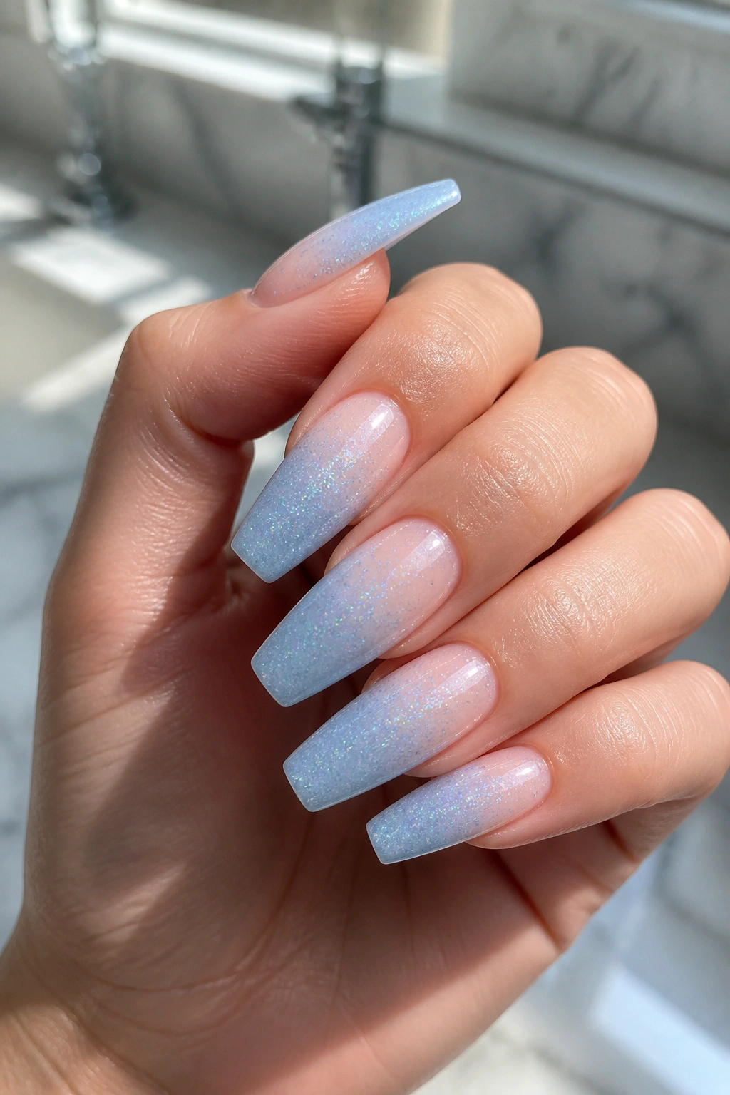 Close-up of coffin nails with blue ombre glitter on a real hand under natural light