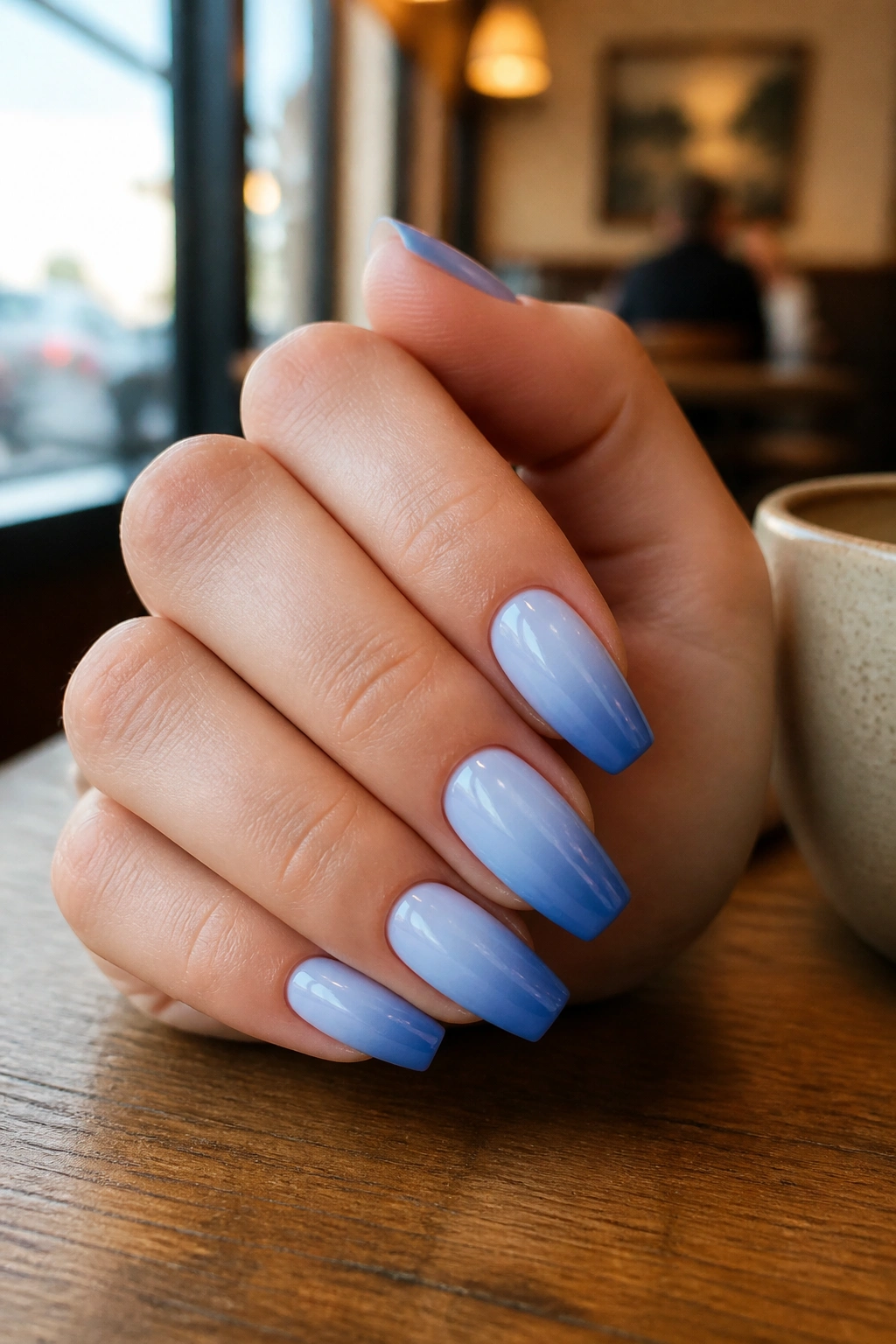 Close-up of short to medium blue ombre coffin nails at a cafe table