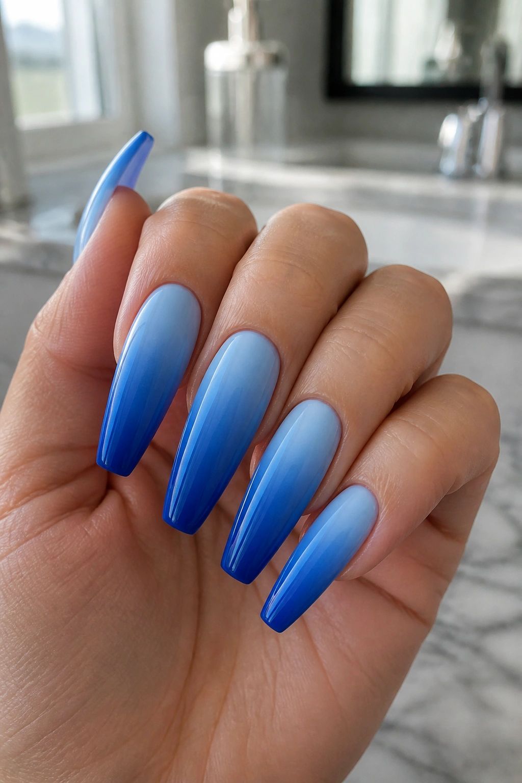 Close-up of blue ombre coffin nails on tapered tips in a bathroom setting