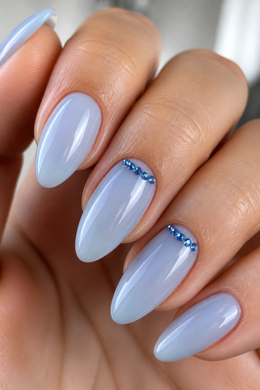 Almond nails with sheer blue base and blue rhinestone crescent near cuticle