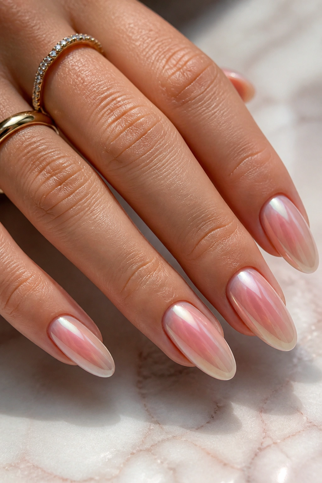 Close-up of almond nails with blush aura chrome on pale pink marble surface.