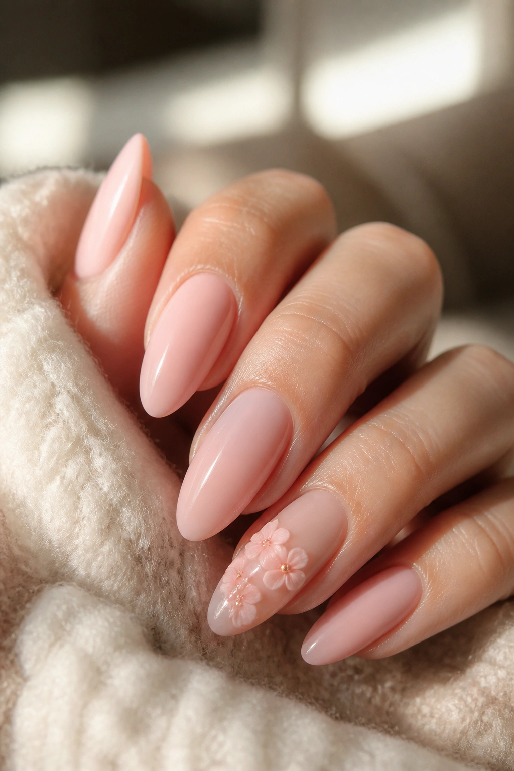 Close-up of blush almond nails with a tiny 3D floral accent on one nail