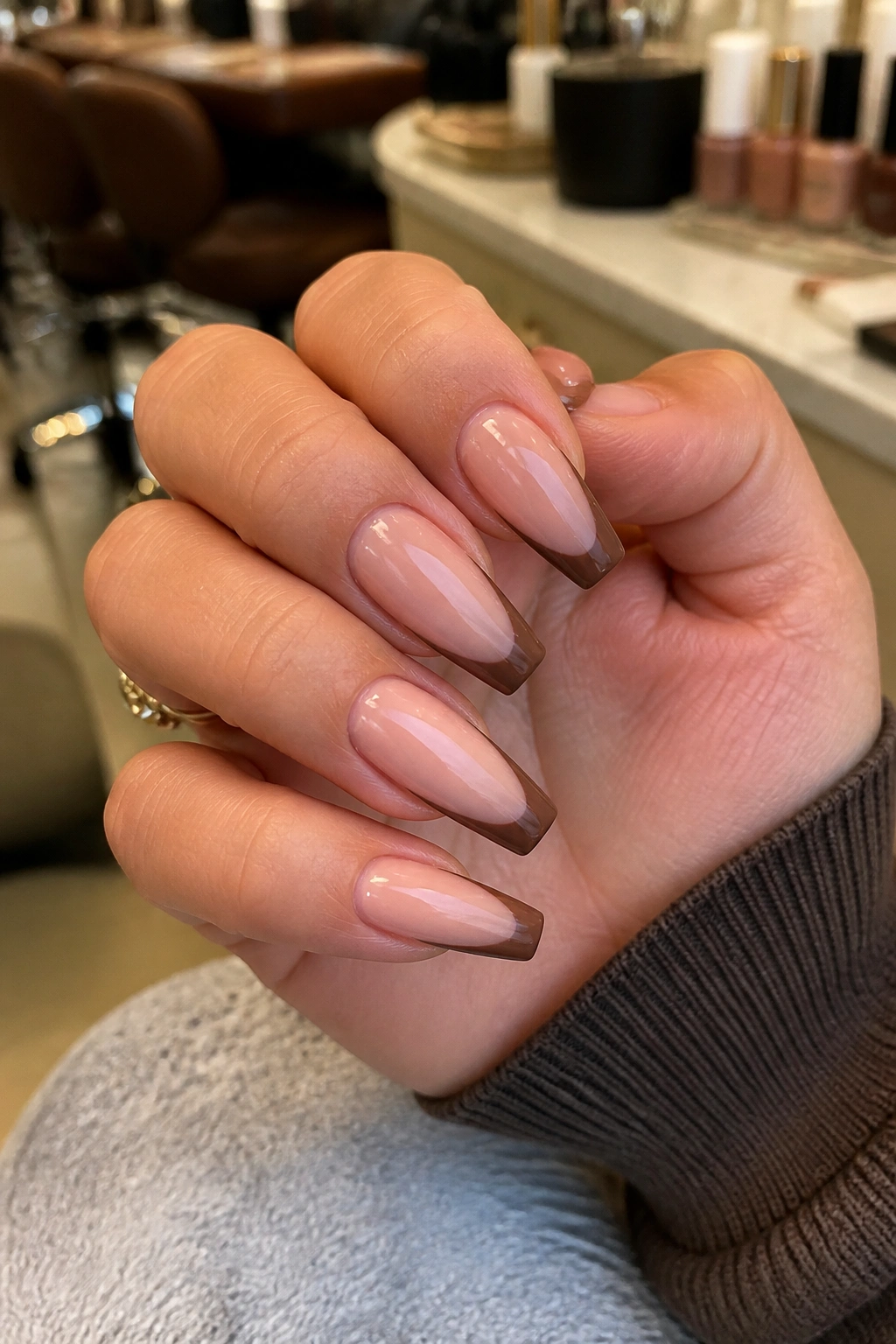 Close-up of brown French tip coffin nails on real hand in salon