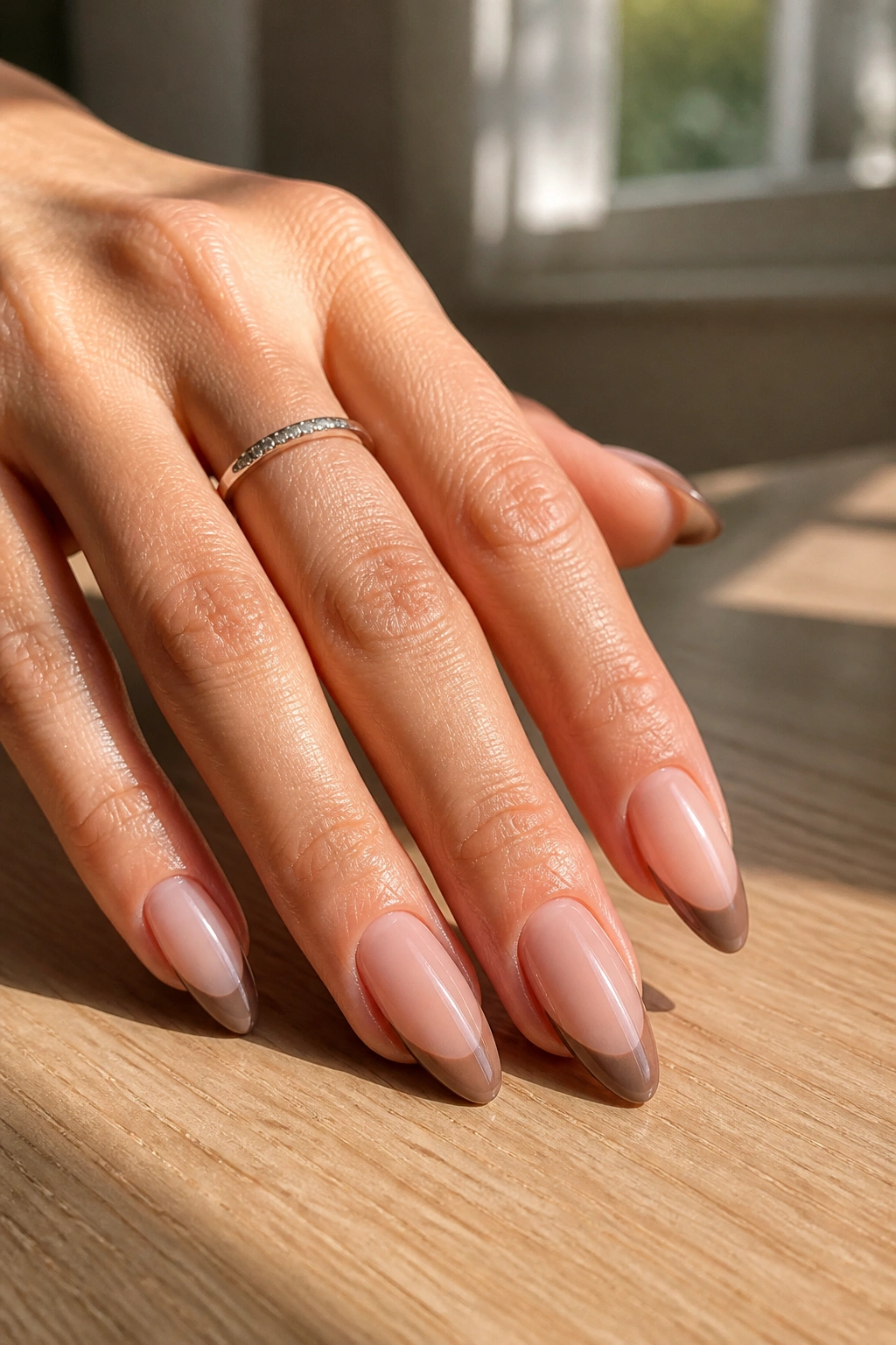 Close-up of almond nails with brown taupe French tips on nude base.
