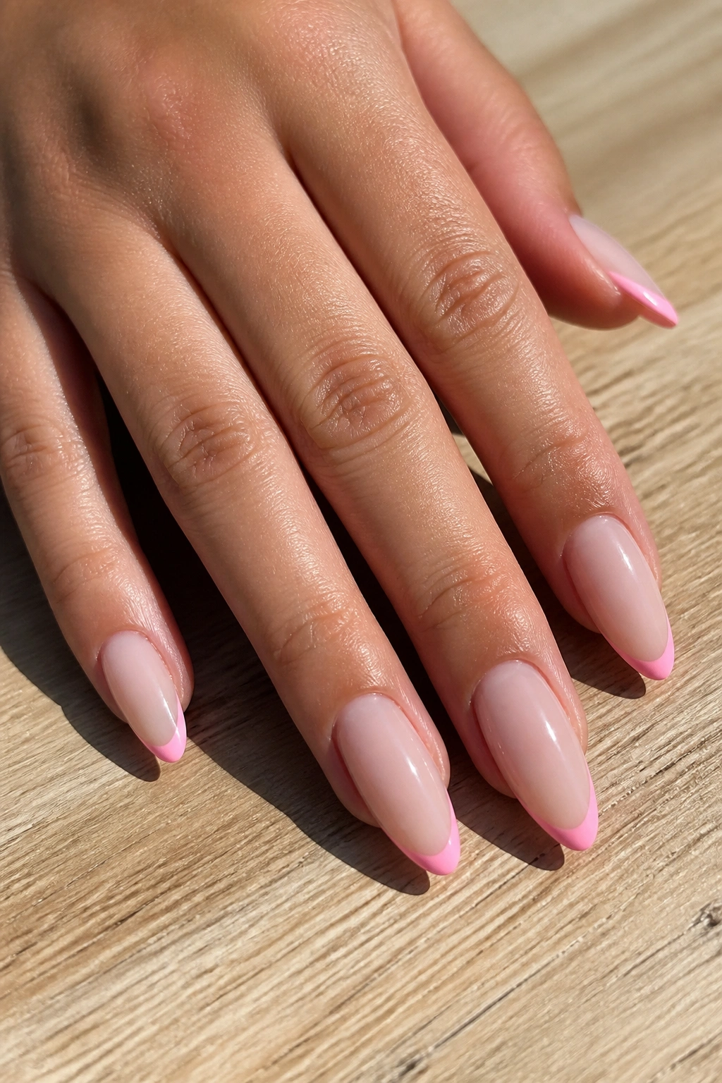 Close-up of a real hand with almond nails featuring bubblegum pink micro French tips