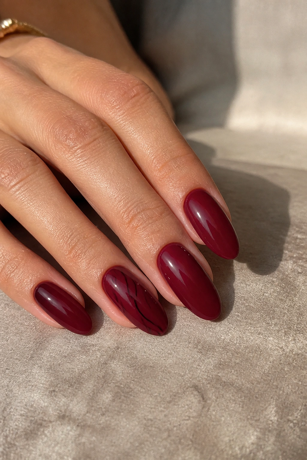 Close-up of burgundy almond nails with subtle black line art on a real woman's hand