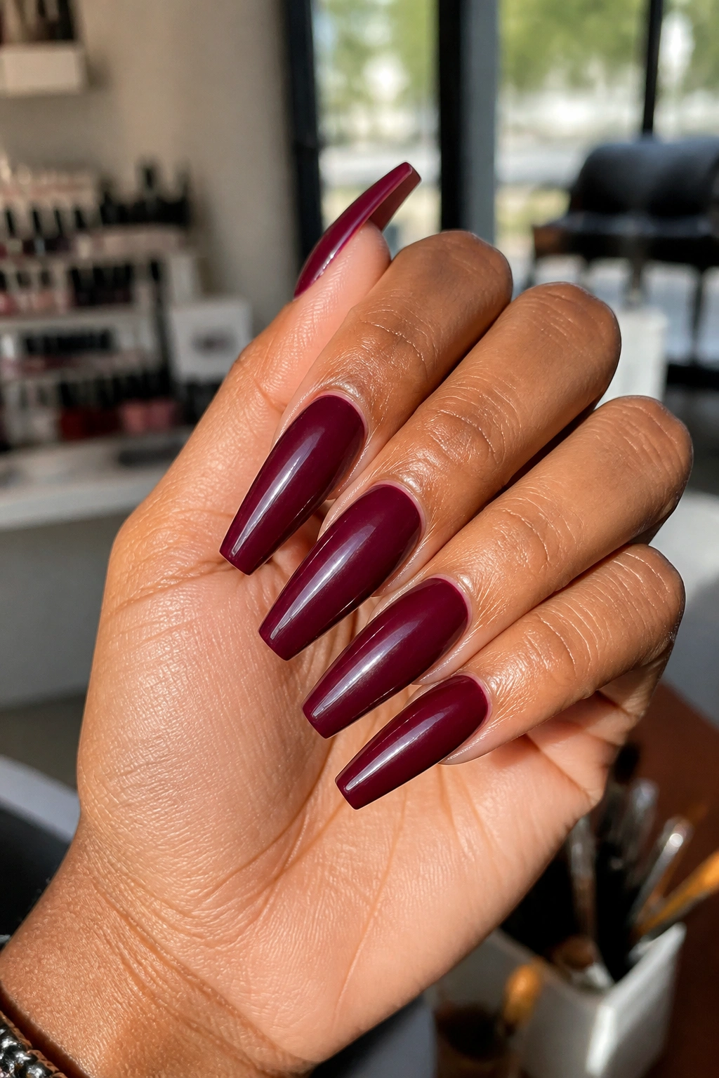 Close-up of burgundy coffin nails on a real hand in a sunlit studio