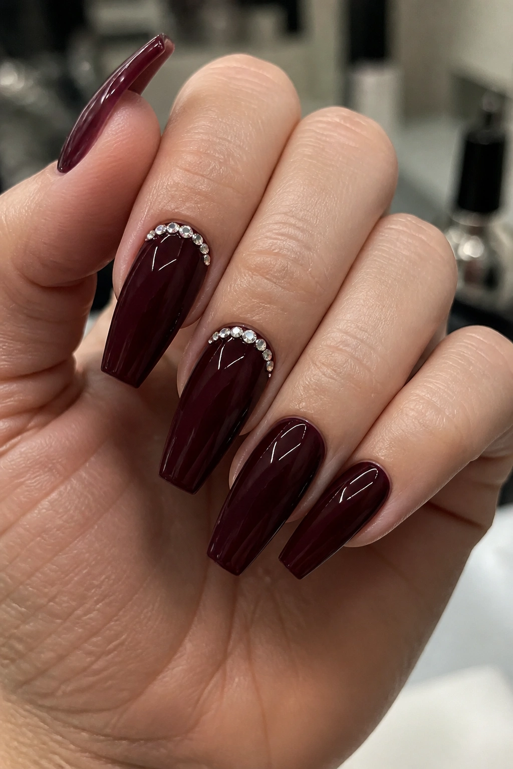Close-up of burgundy coffin nails with tiny crystals near cuticle on real hand