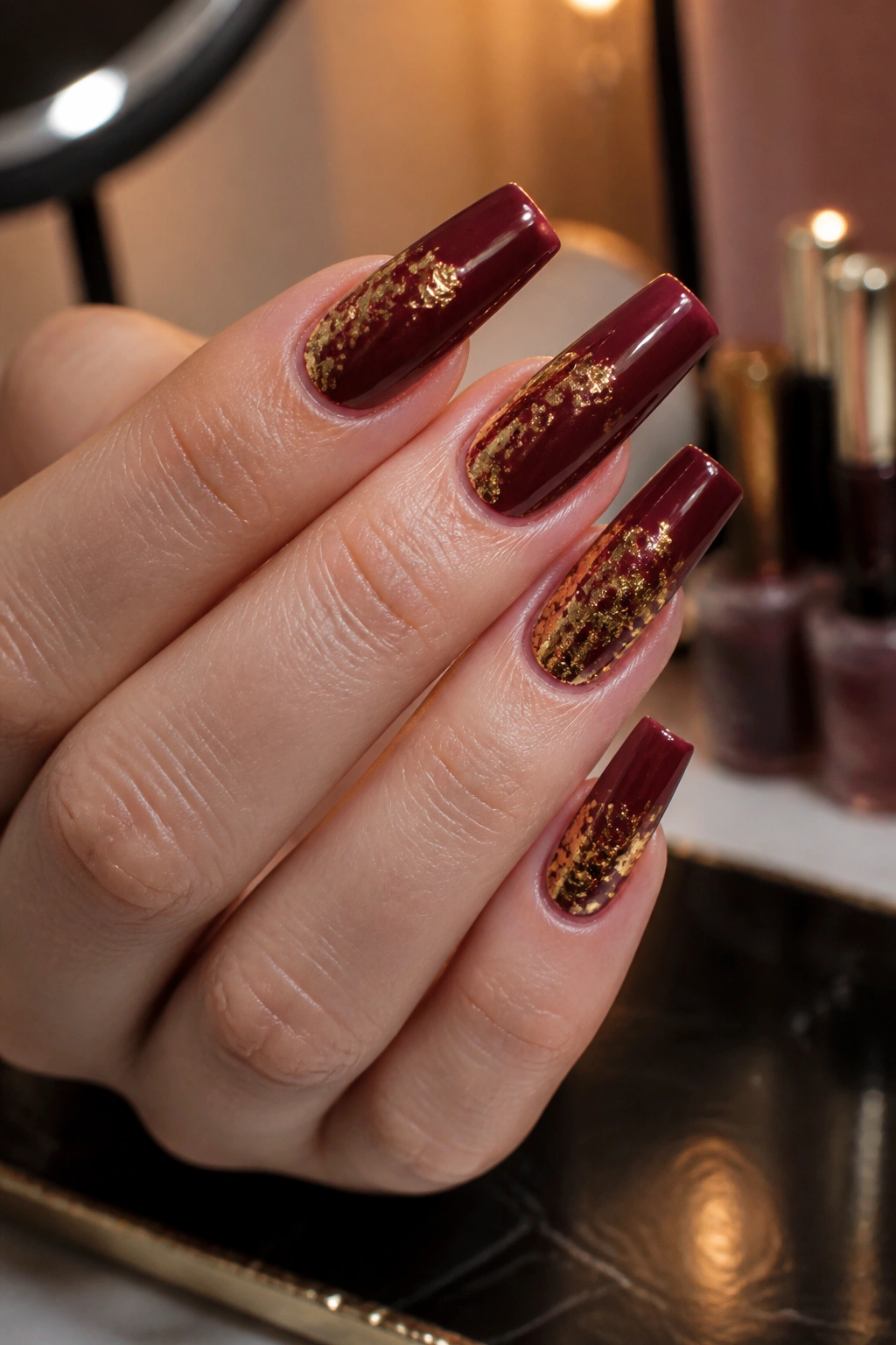 Close-up of burgundy coffin nails with subtle gold foil accents on a real hand