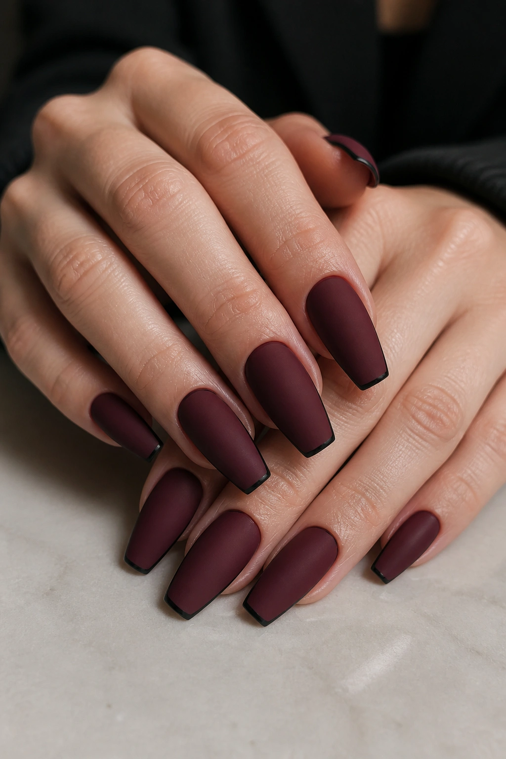 Close-up of burgundy matte coffin nails with a hairline black micro-French edge on real hands