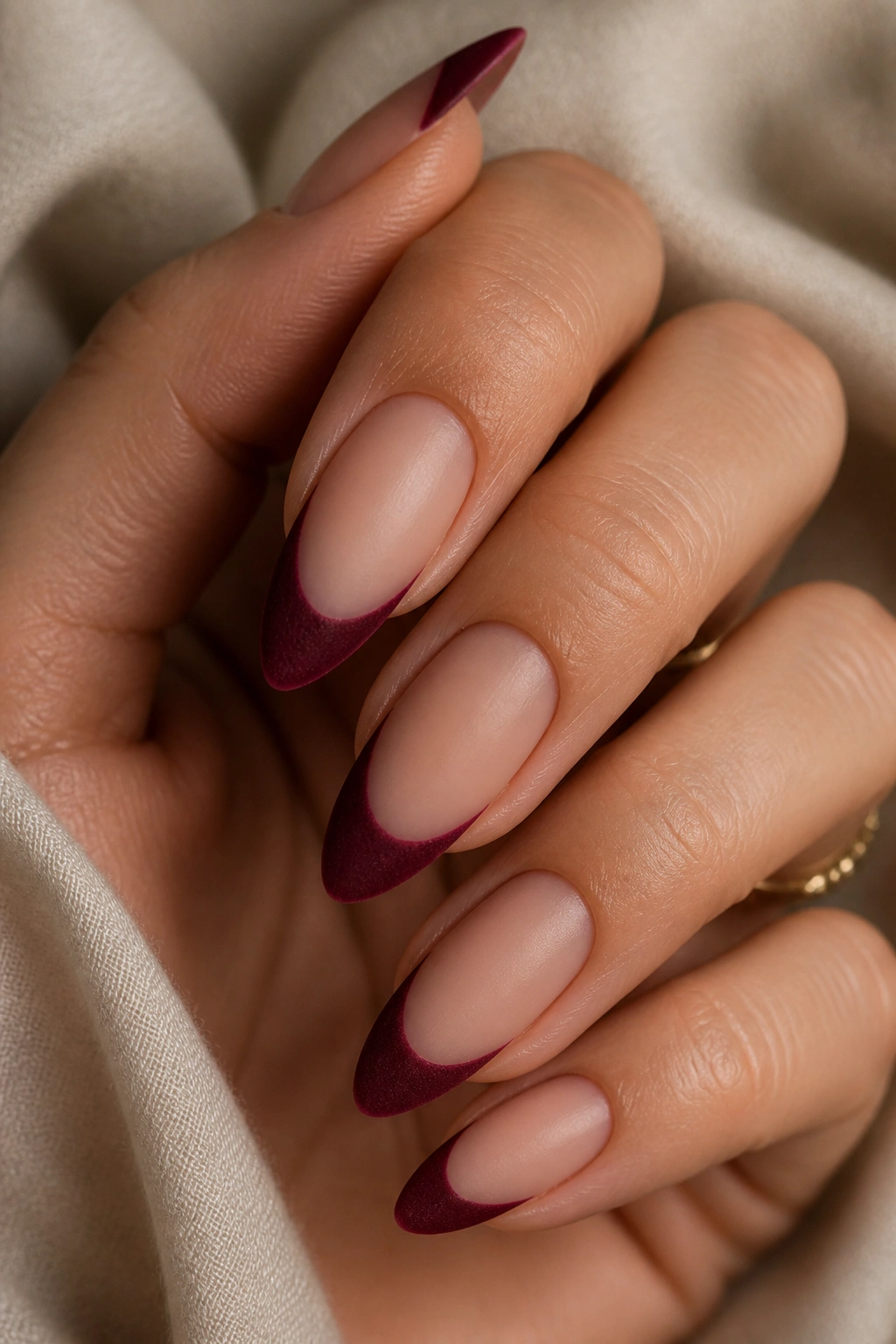 Close-up of burgundy velvet almond nails with French tips on a nude base