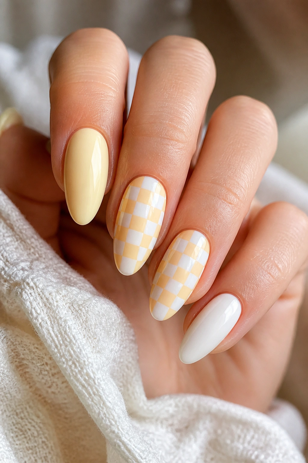 Almond nails with small yellow and white checkerboard accents on two nails.