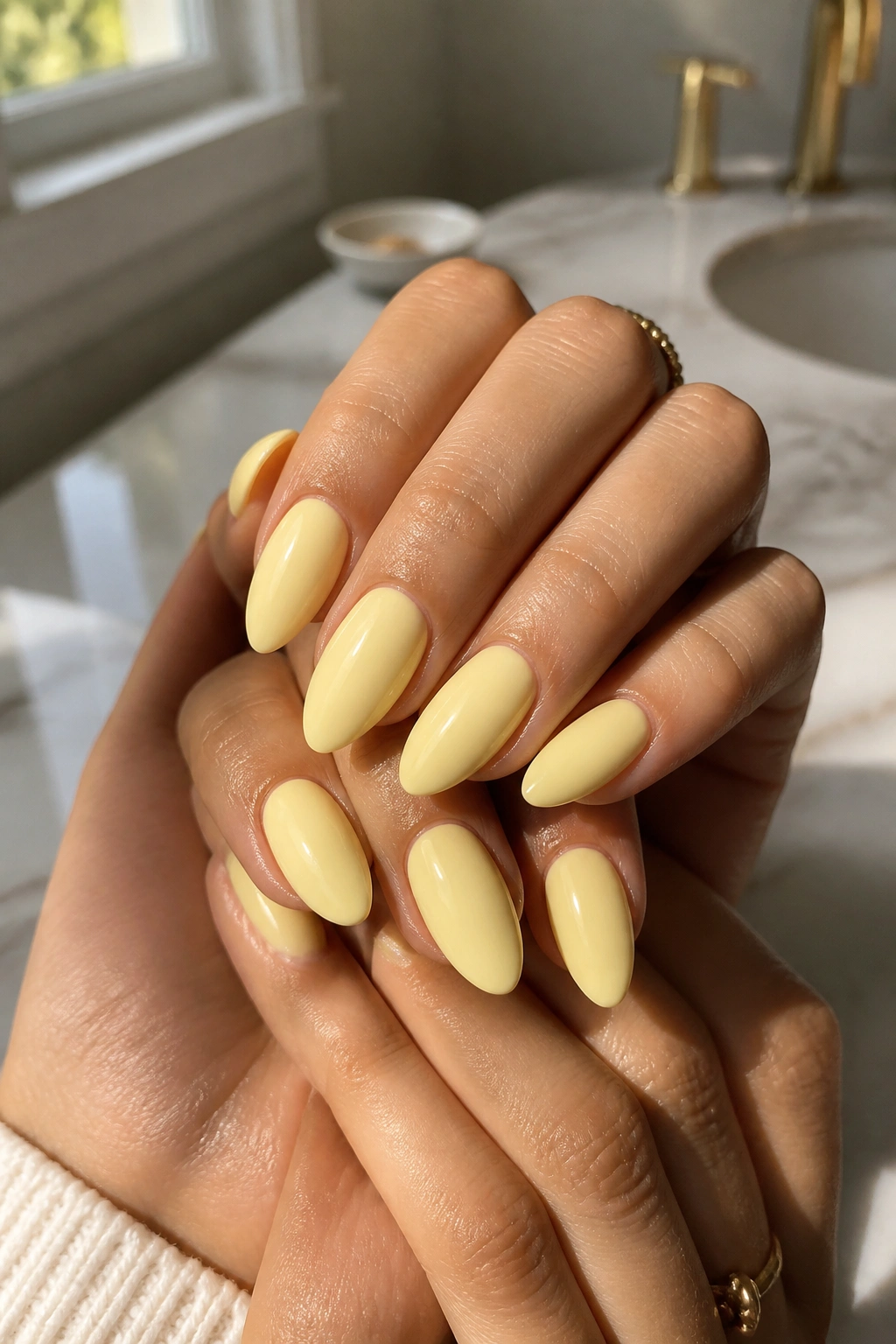 Close-up of creamy butter-yellow almond nails on a real person’s hands with a glossy finish in natural window light