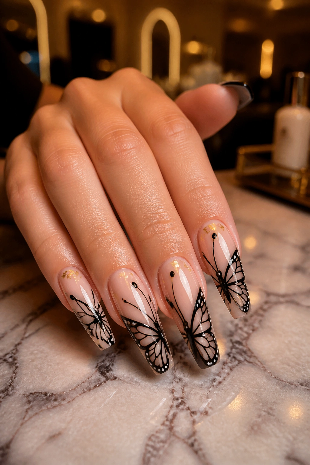Close-up of black and nude butterfly coffin nails with gold foil on a real hand in a luxury salon