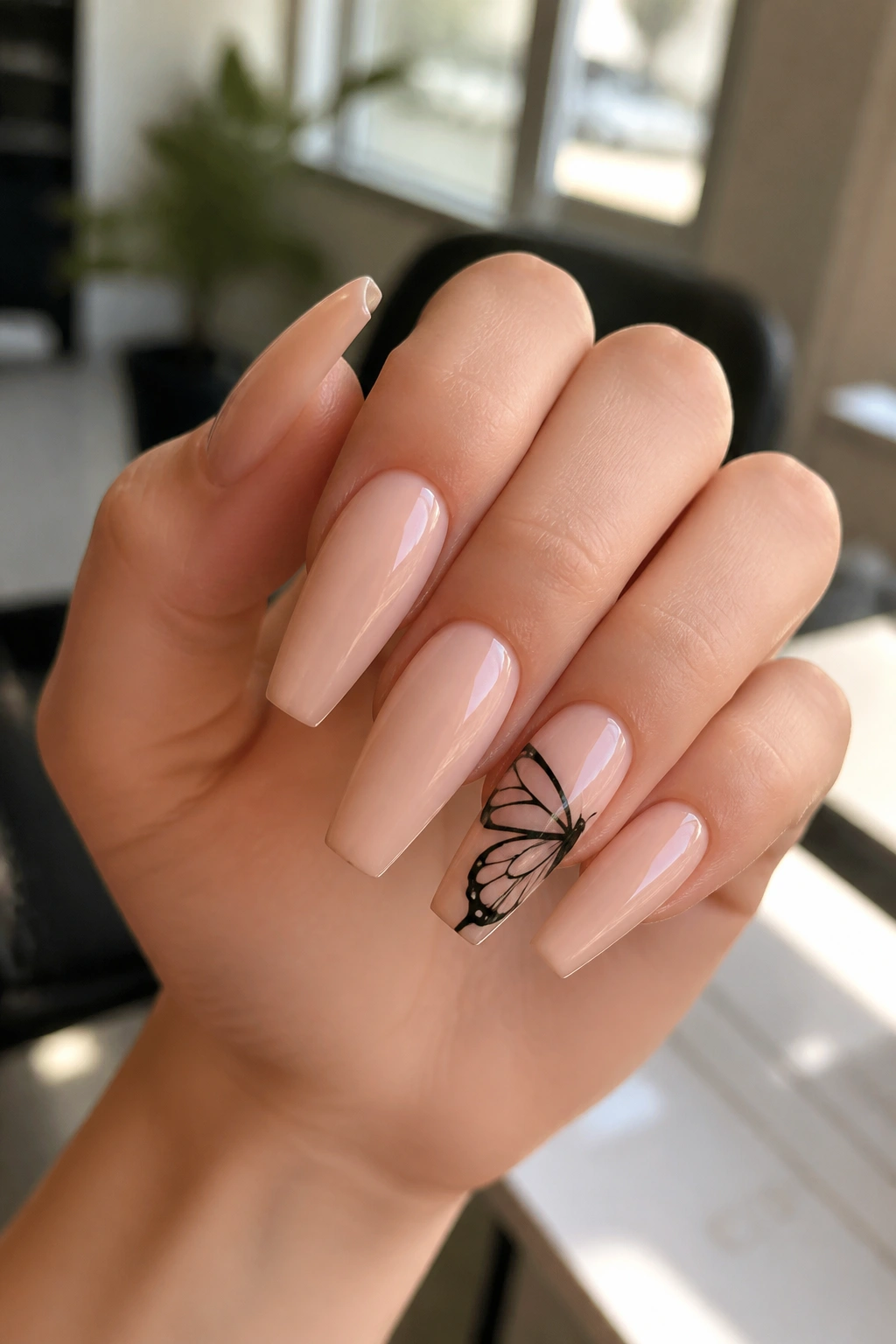 Close-up of tapered coffin nails with butterfly wing art on a real hand in soft salon light
