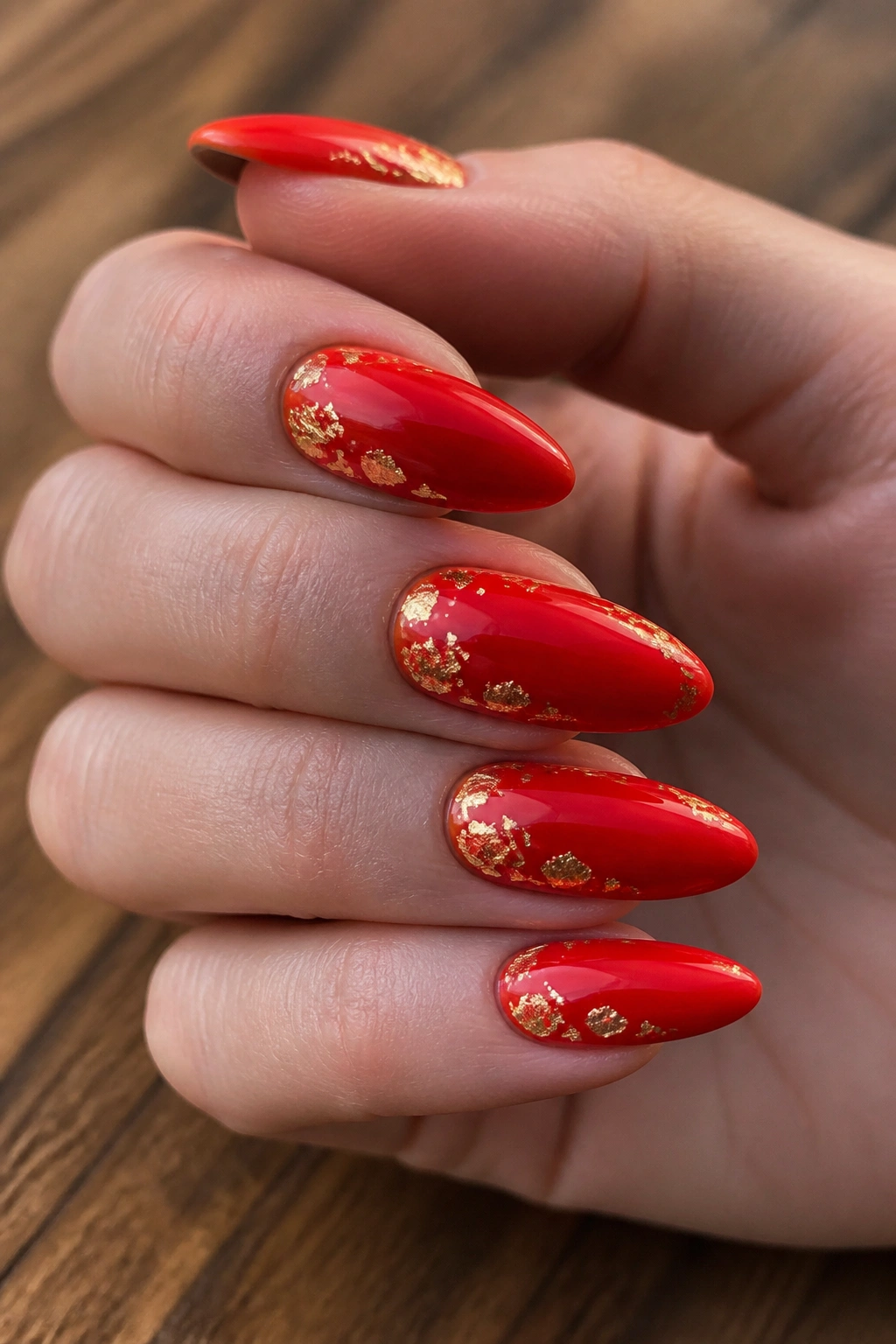 Close-up of long almond nails with candy apple red polish and gold foil accents