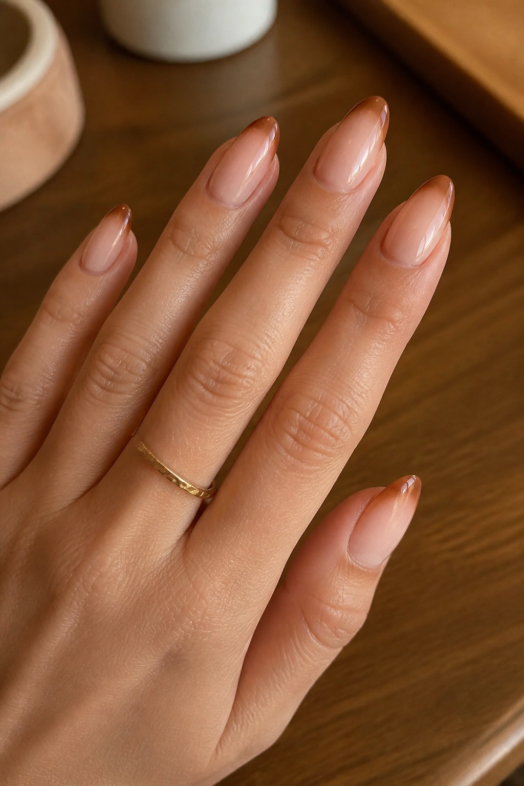 Close-up of a real hand with almond nails featuring a caramel fade French tip
