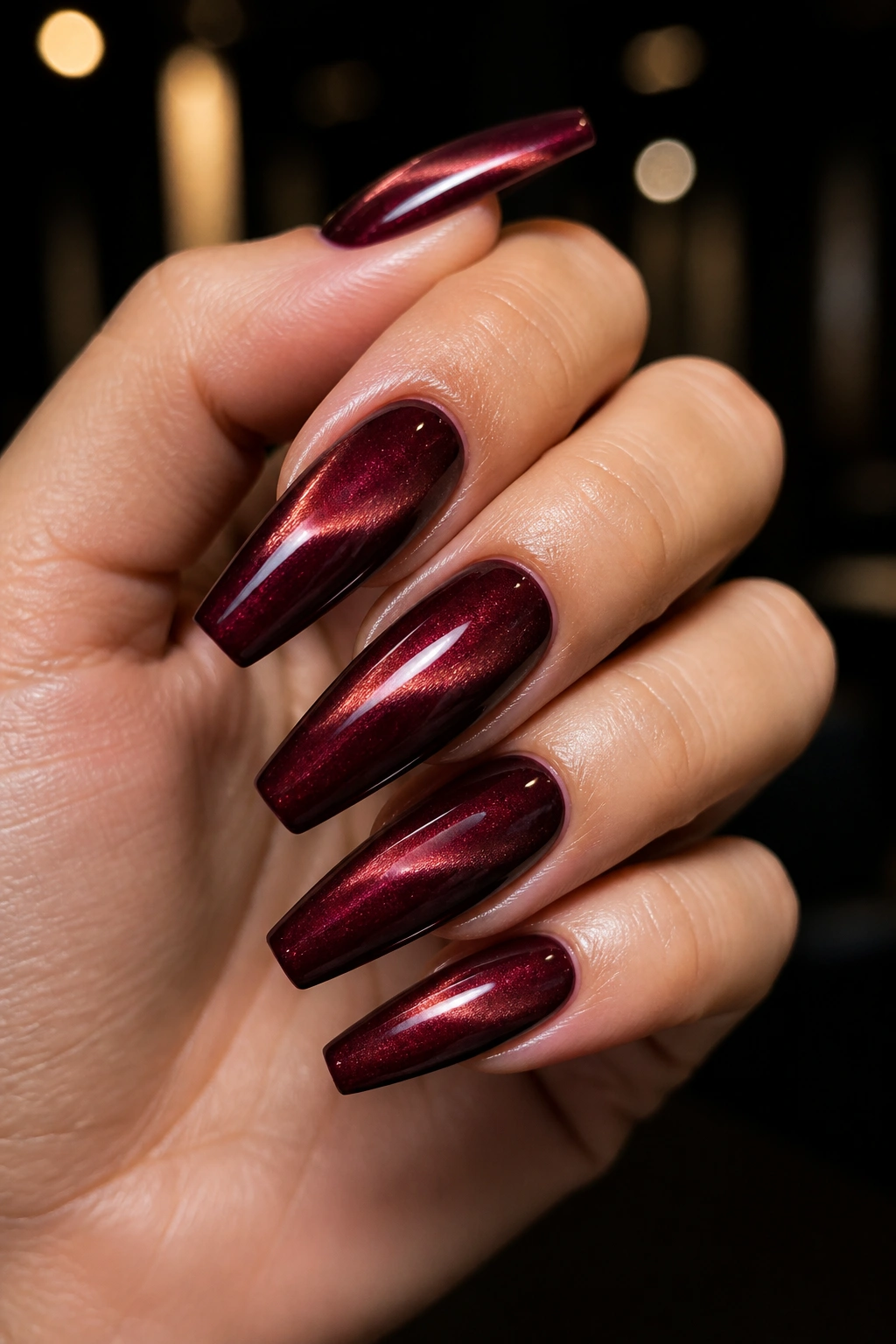 Close-up of velvet cat-eye burgundy coffin nails on a real hand