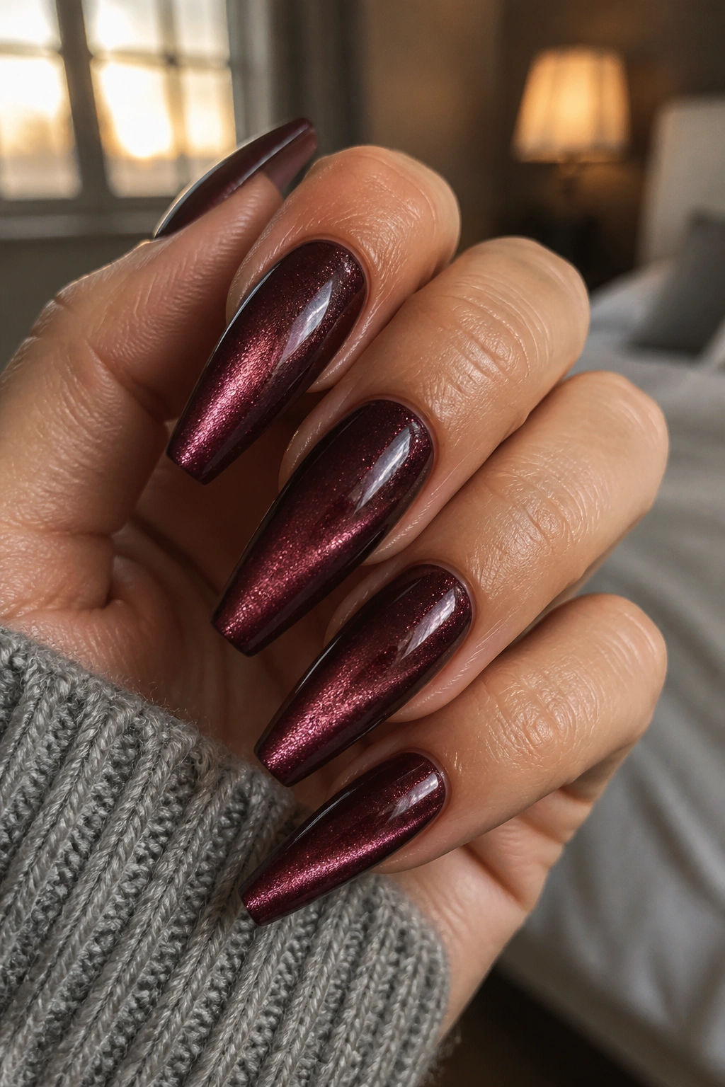 Close-up of velvet cat-eye maroon coffin nails on real hand.